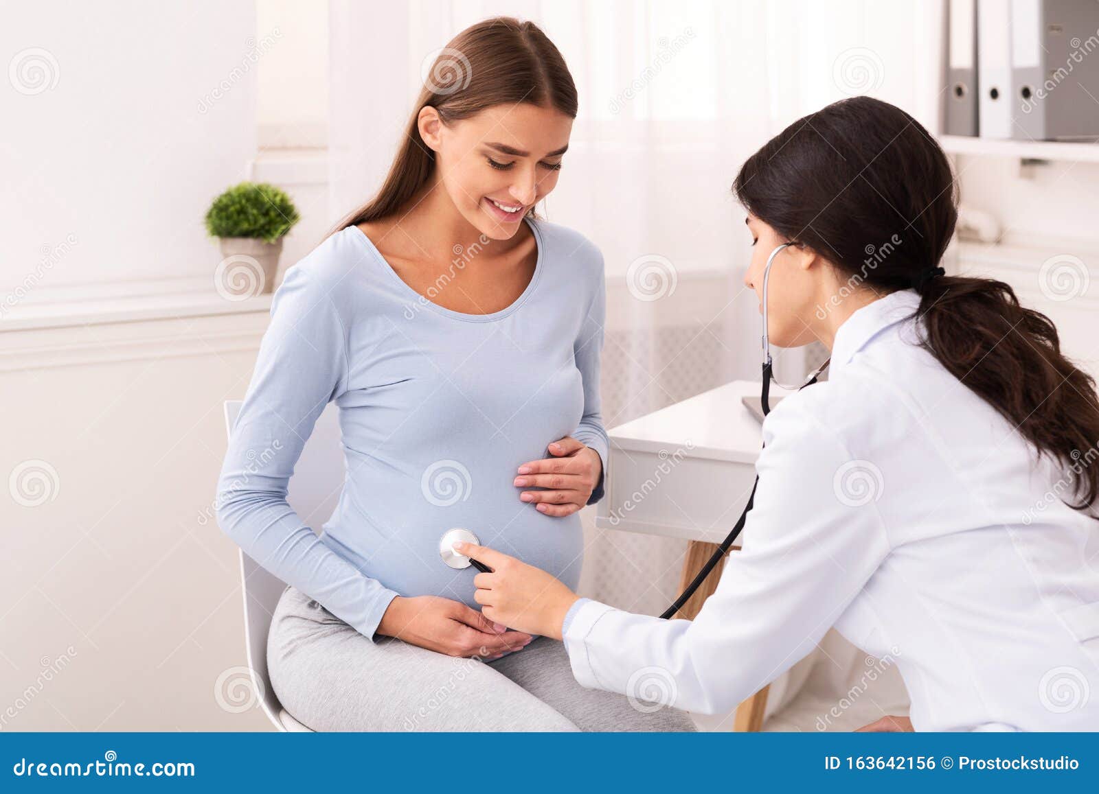 doctor examining pregnant woman holding stethoscope near belly in office