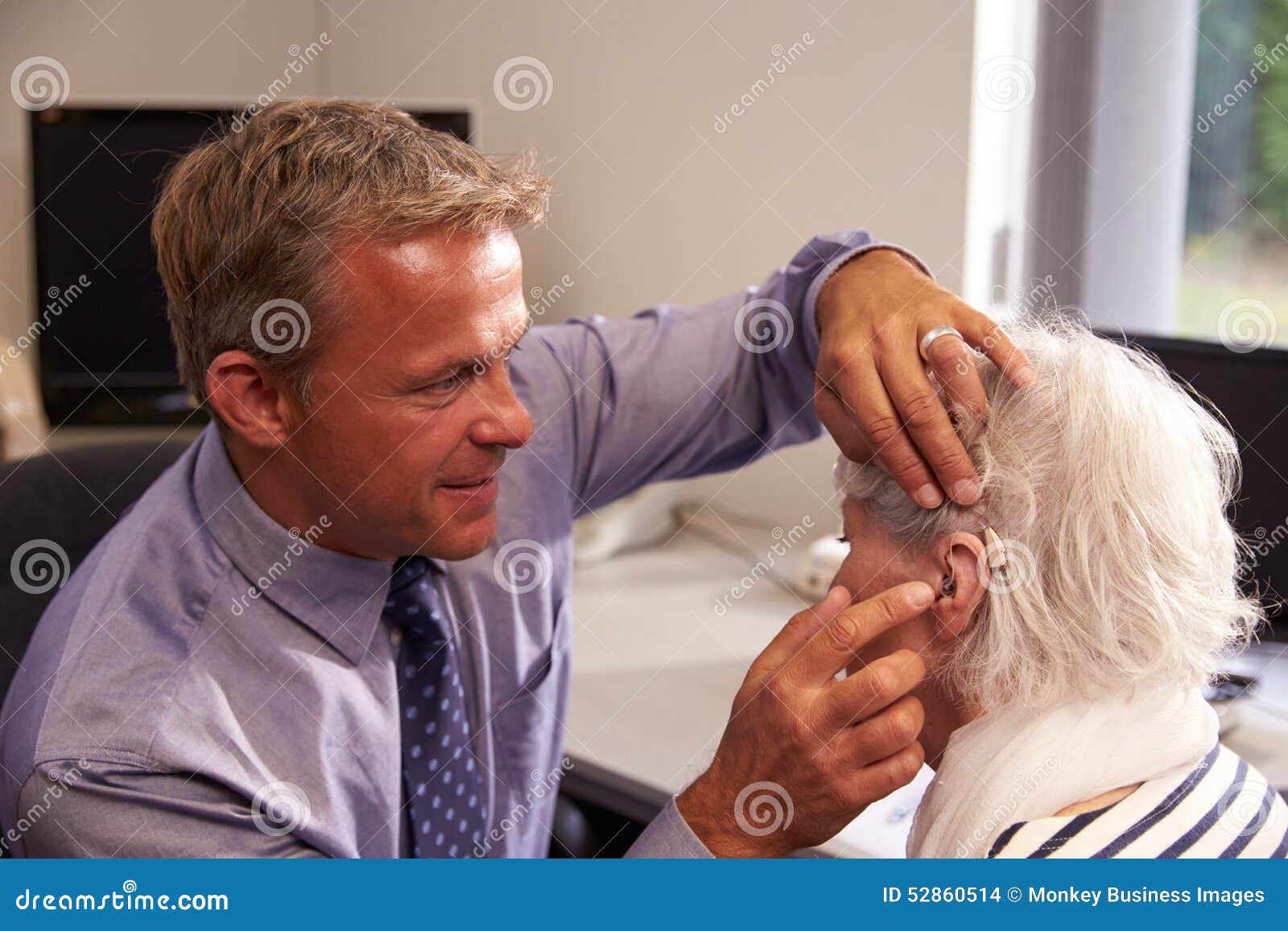 doctor fitting senior female patient with hearing aid