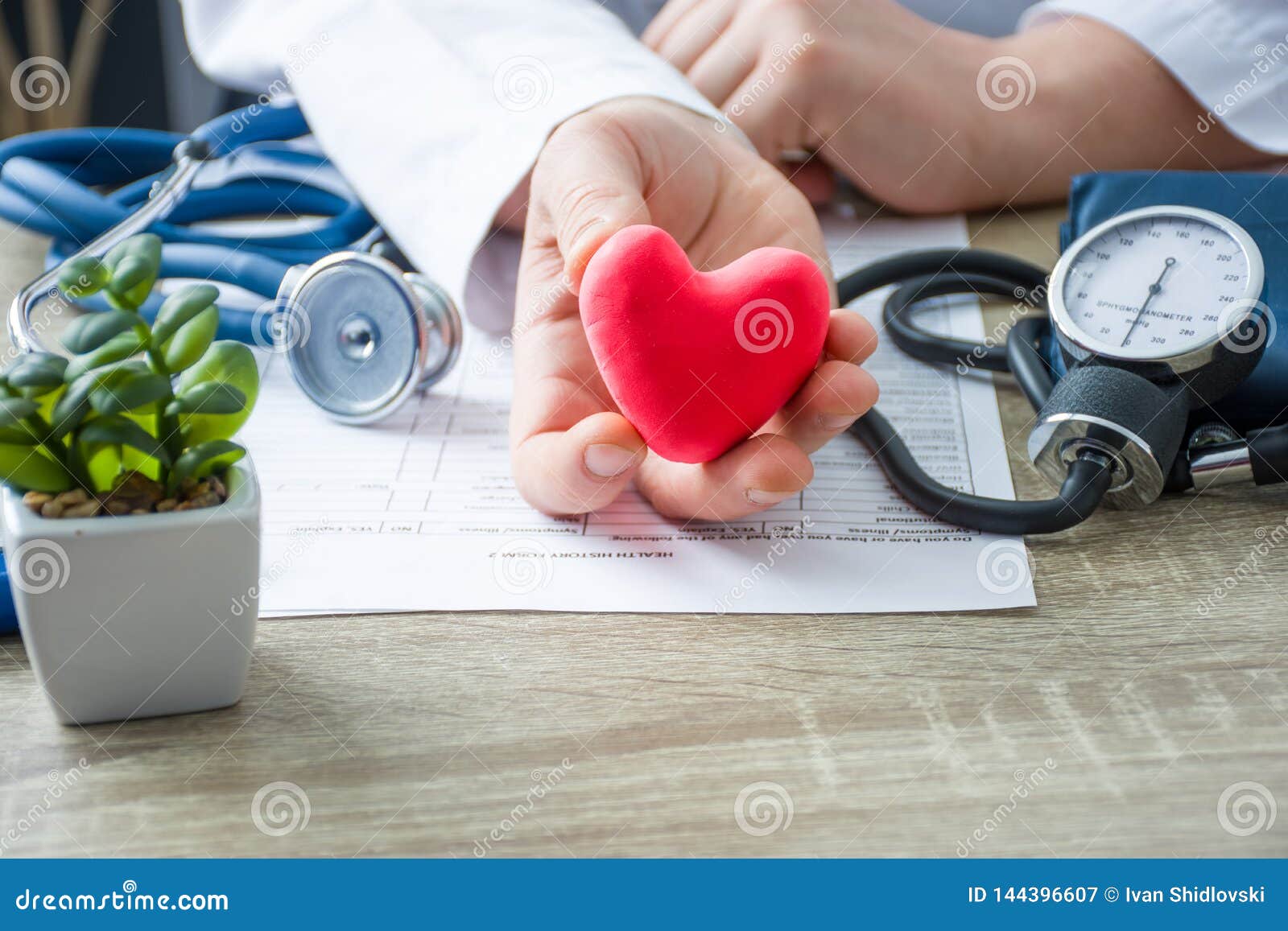 doctor of internal medicine and cardiologist holding in his hands and shows to patient figure of red card heart during medical con