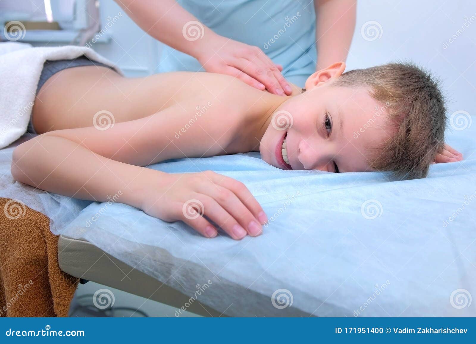 doctor massagist making therapeutic massage to teen boy on spine in clinic.