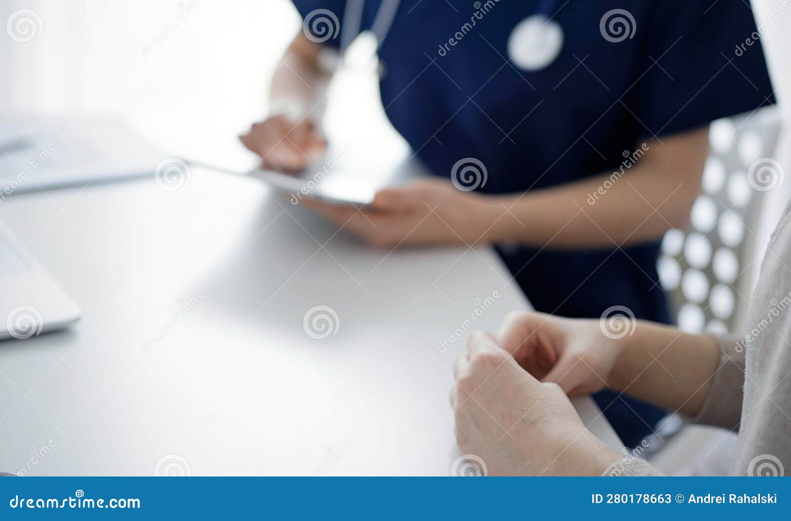 doctor and patient sitting at the table in clinic while discussing something and using tablet computer. the focus is
