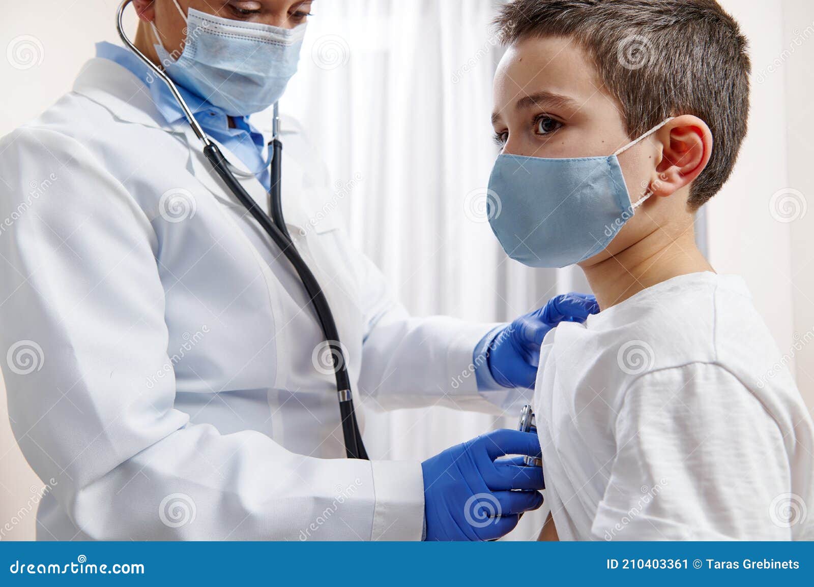 doctor pediatrician in medical uniform uses a stethoscope while auscultating a little boy in protective medical mask