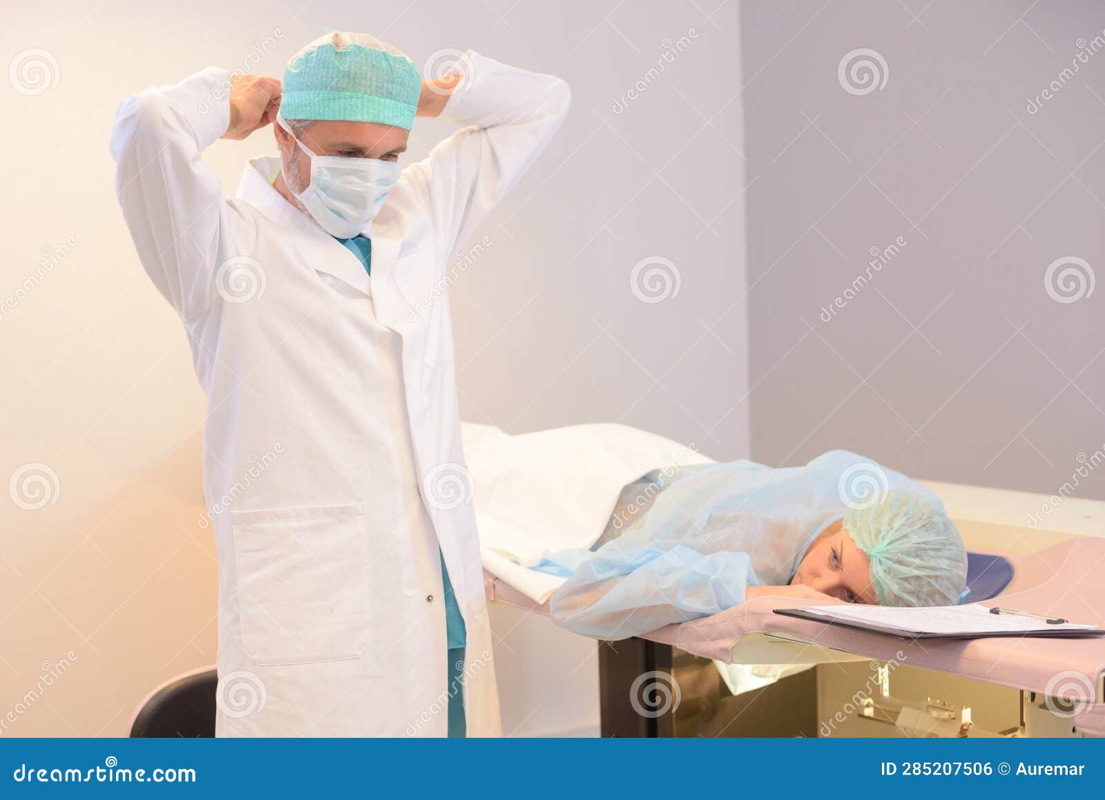 Doctor Putting on Mask Patient Laying Face Down on Bed Stock Photo