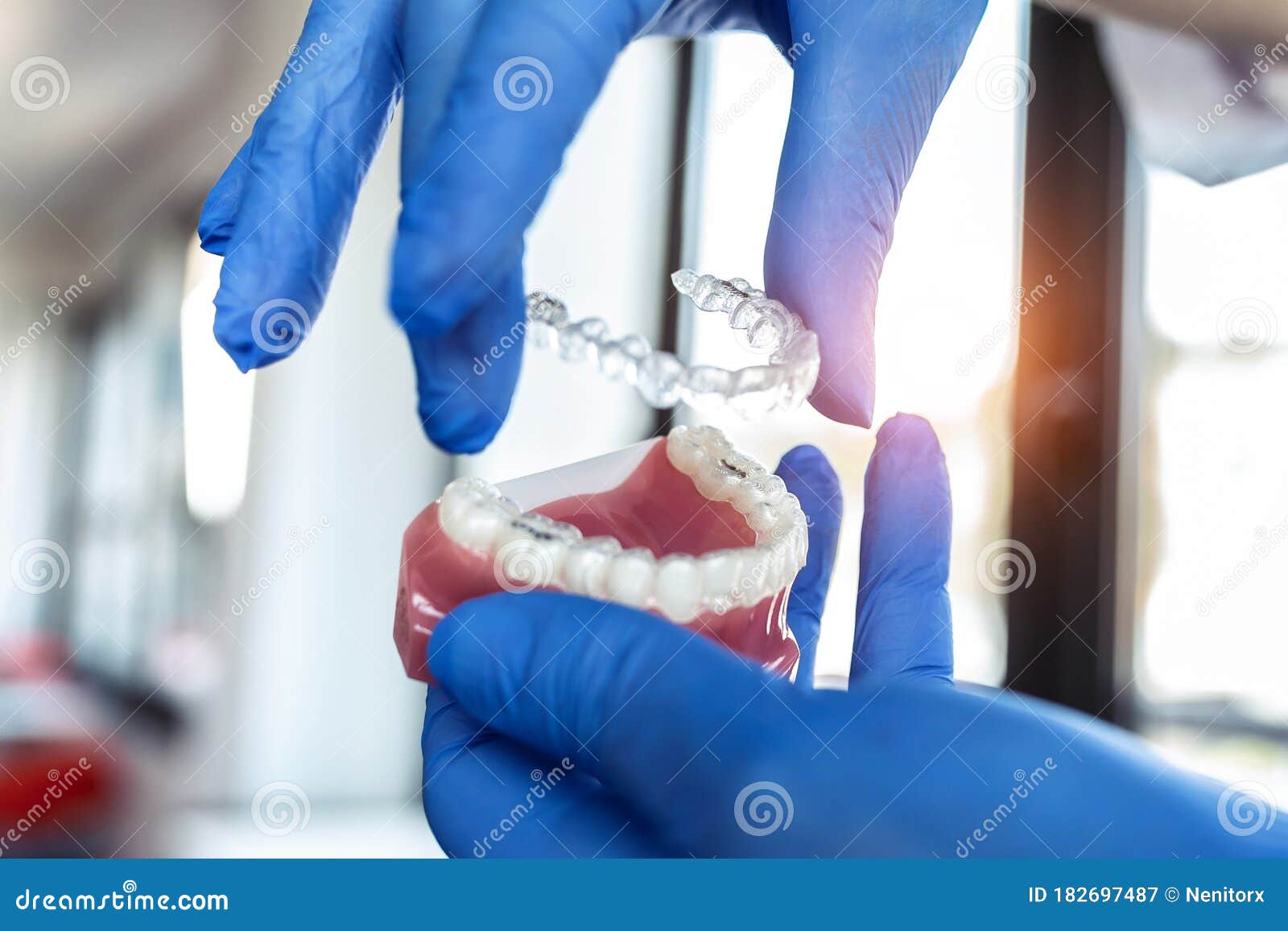 the doctorÃ¢â¬â¢s hands in blue gloves hold an artificial model of the jaw with invisible braces. the dentist shows an example of