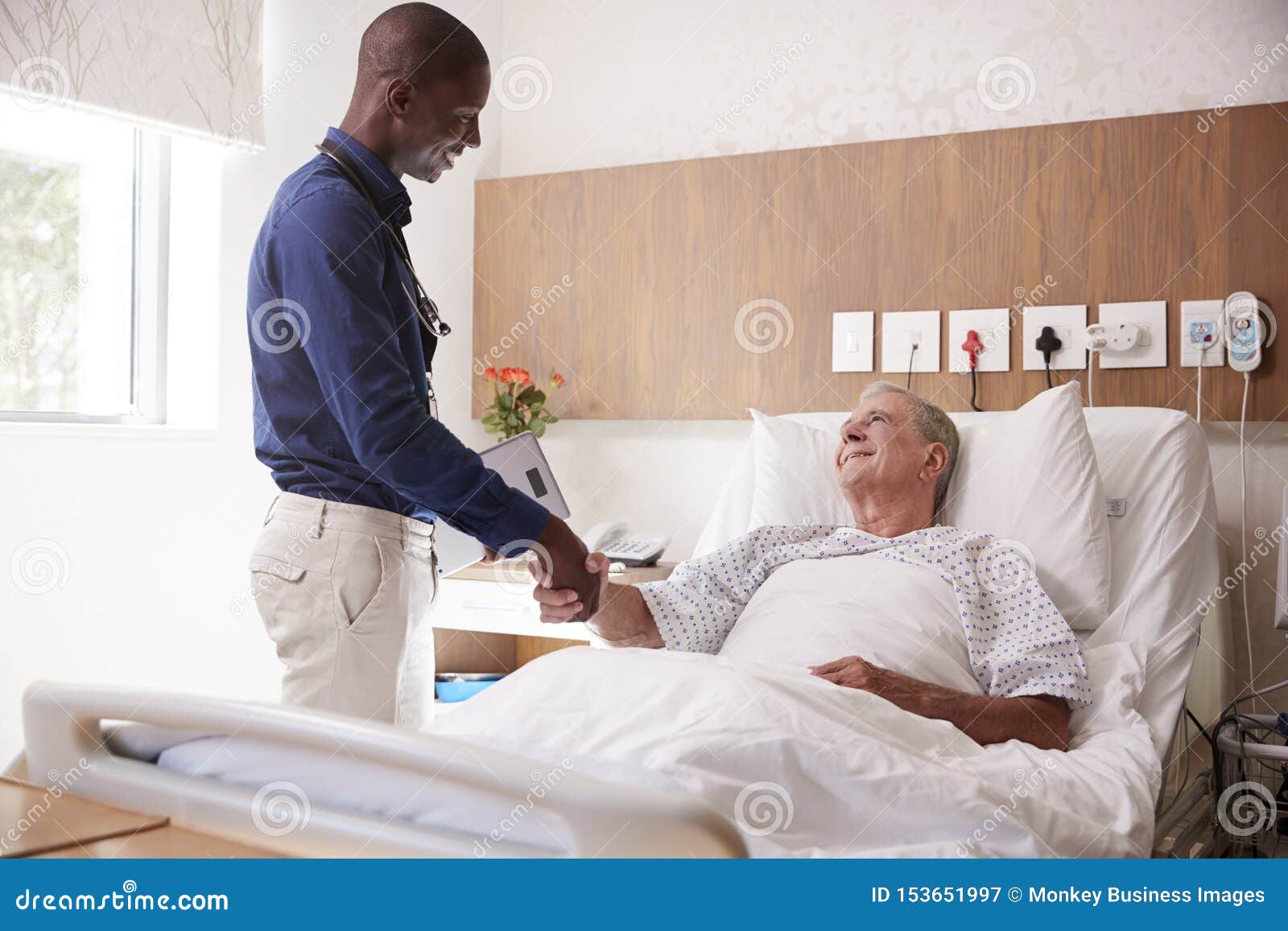 doctor shaking hands with senior male patient in hospital bed in geriatric unit