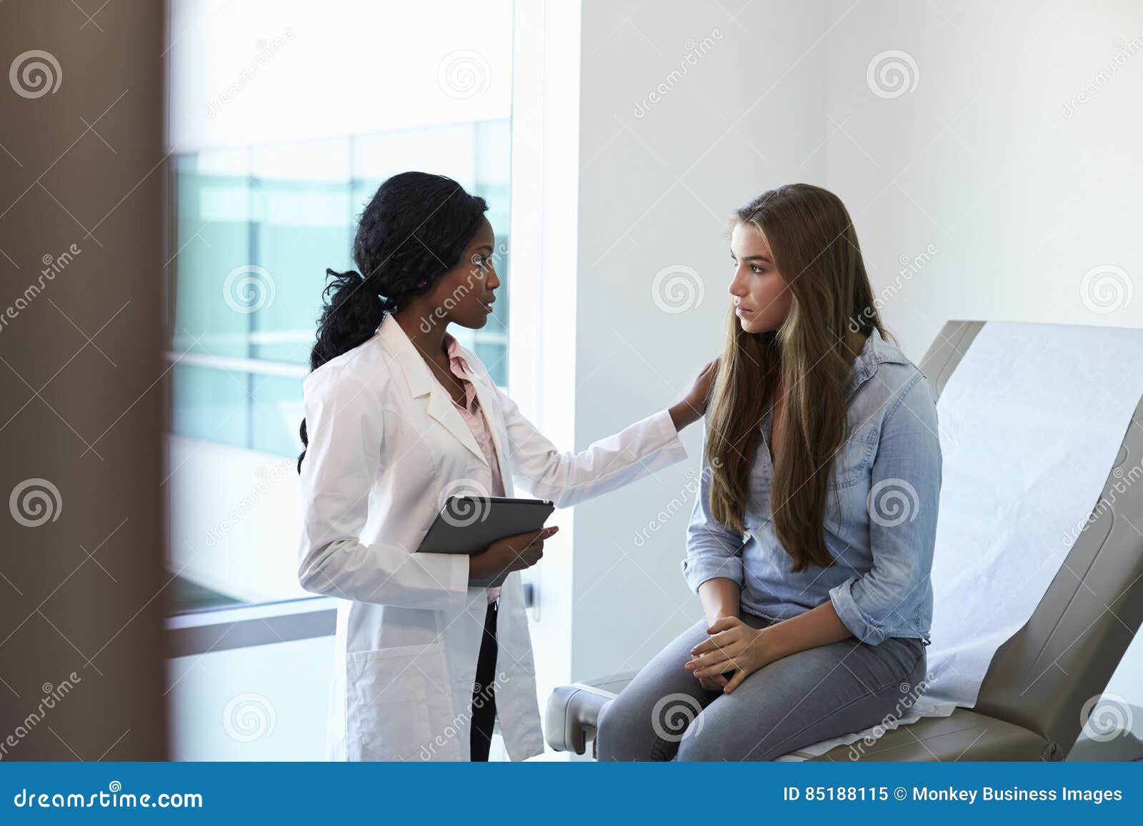 doctor talking to unhappy teenage patient in exam room