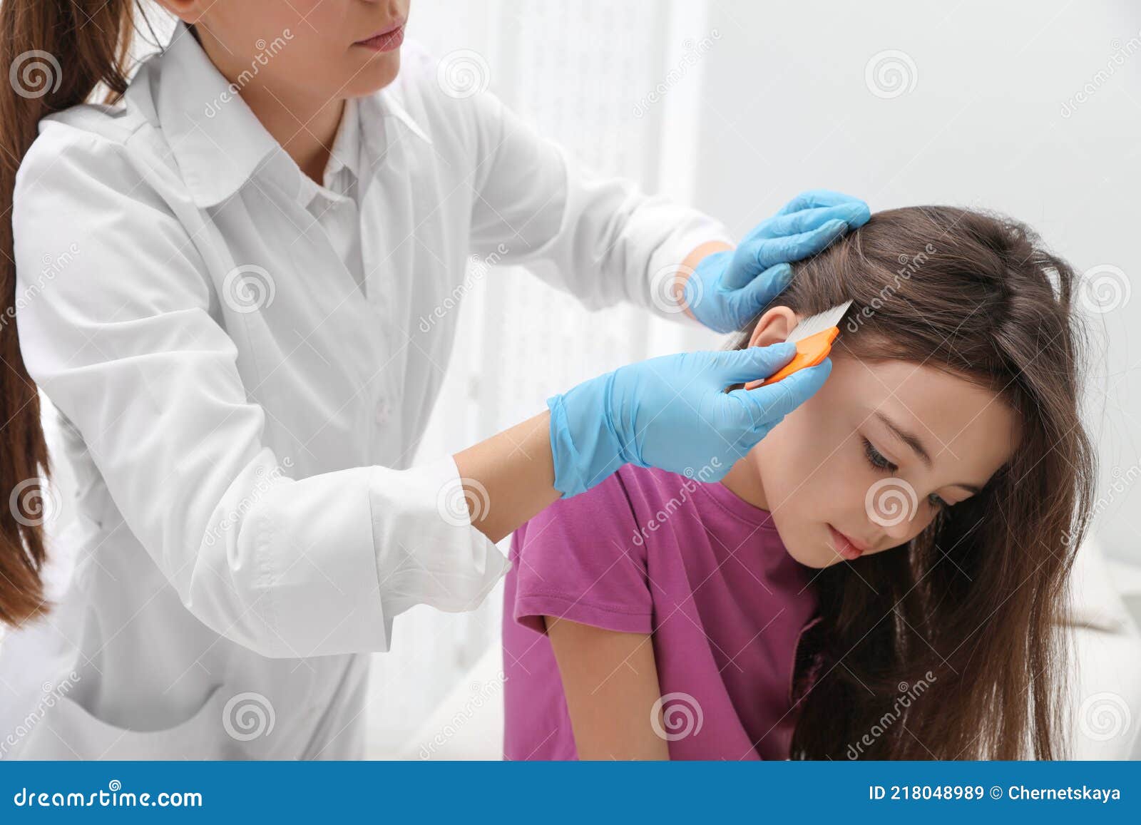 doctor using nit comb on little girl`s hair indoors. anti lice treatment