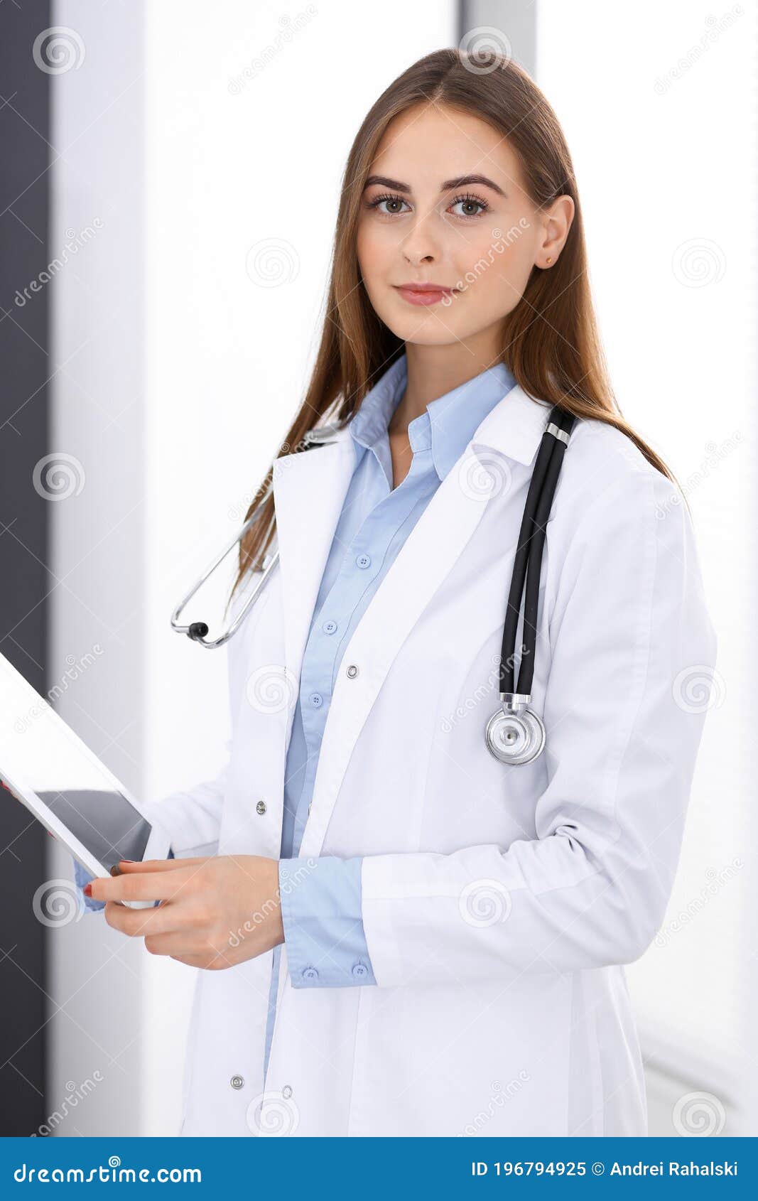 doctor woman using tablet computer while standing straight near window in hospital. happy physician at work. medicine