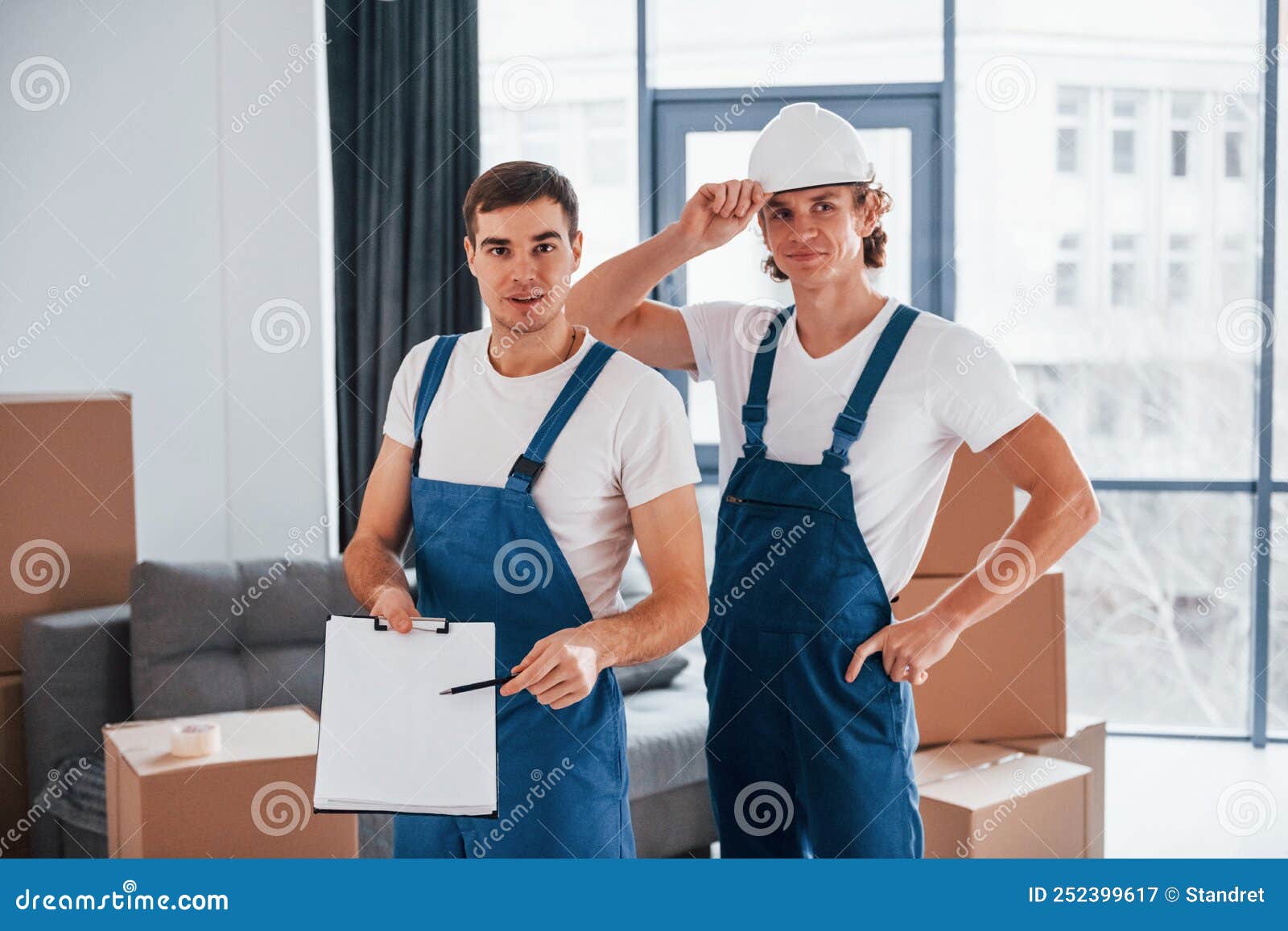 Document To Sign. Two Young Movers in Blue Uniform Working Indoors in