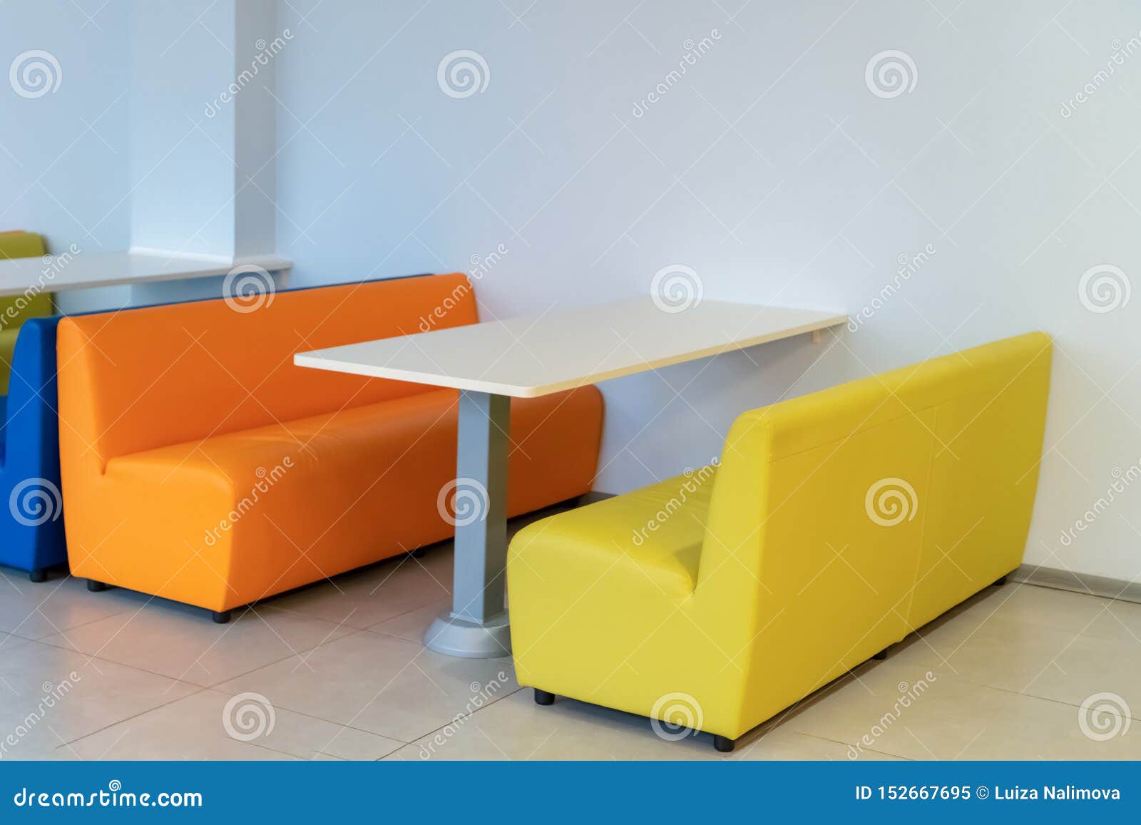 Dois sofás coloridos das poltronas com uma tabela na sala Benchs amarelos e alaranjados Design de interiores escola