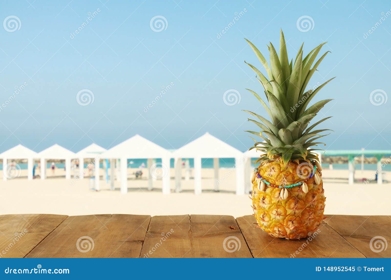 Ripe pineapple over wooden table in front of beach and tropical background.