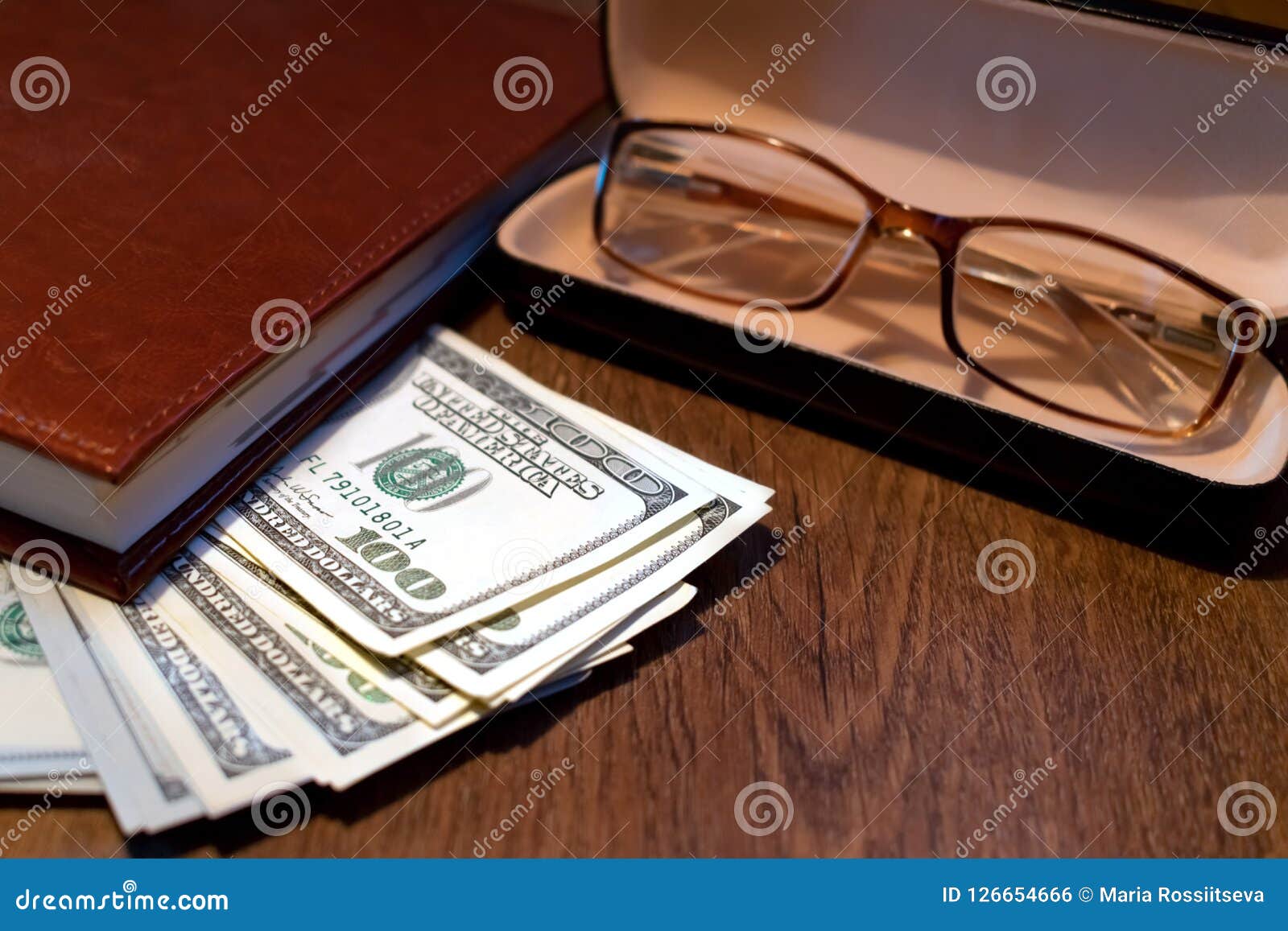 Dolary i szkła na stole. Sterta sto dolarowych rachunków pod notatnikiem z szkłami w skrzynce na drewnianym stole