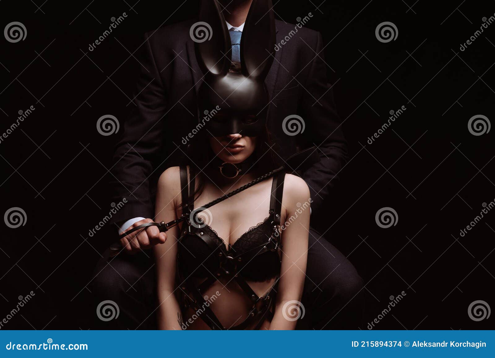 Dominant Man with a Flogger Whip and a Submissive Girl in a Mask and Leather Belt Stock Photo picture