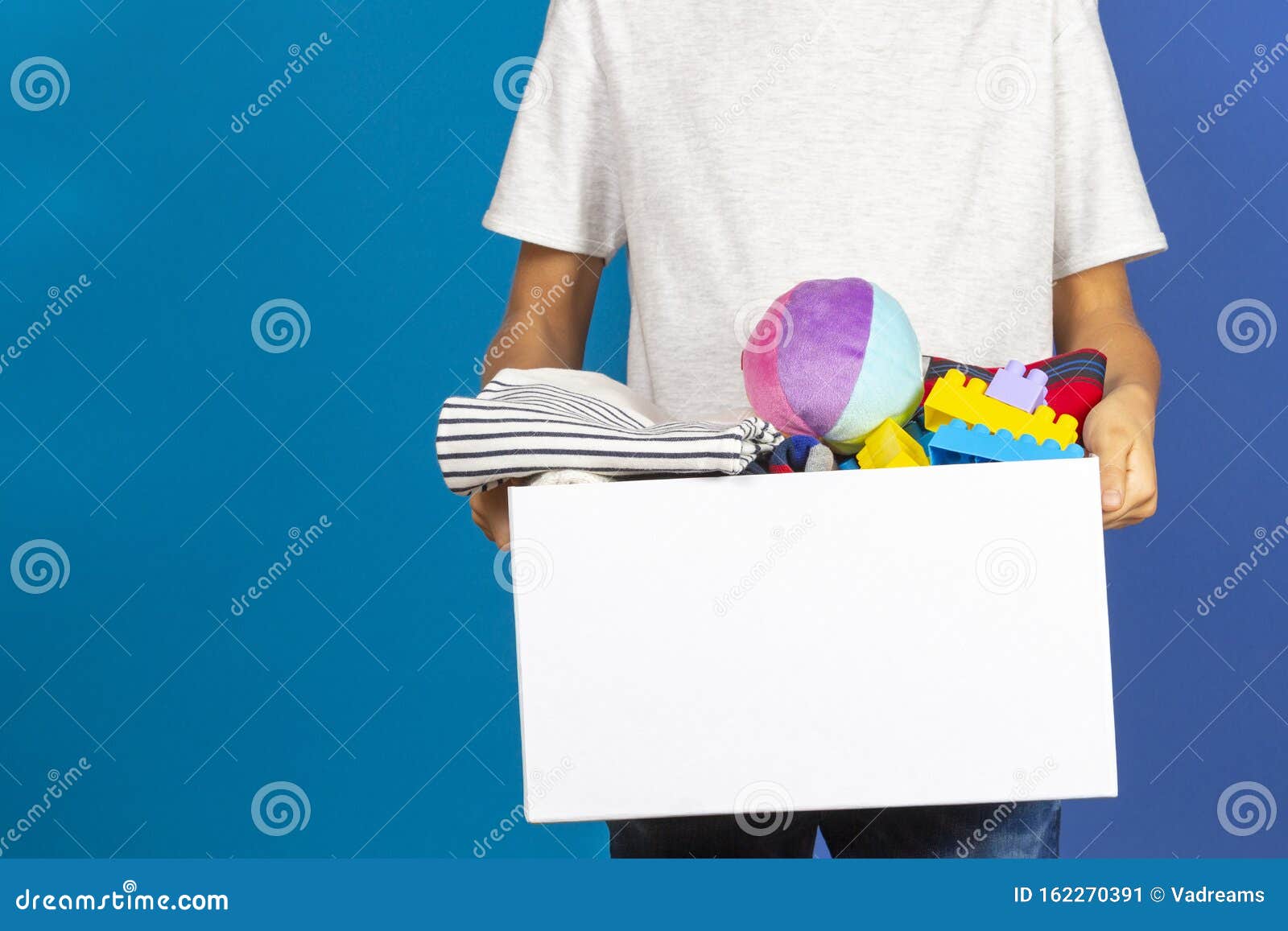 Donation Concept. Kid Hands Holding Donate Box Full Of Books, Clothes And Toys Near Blue ...