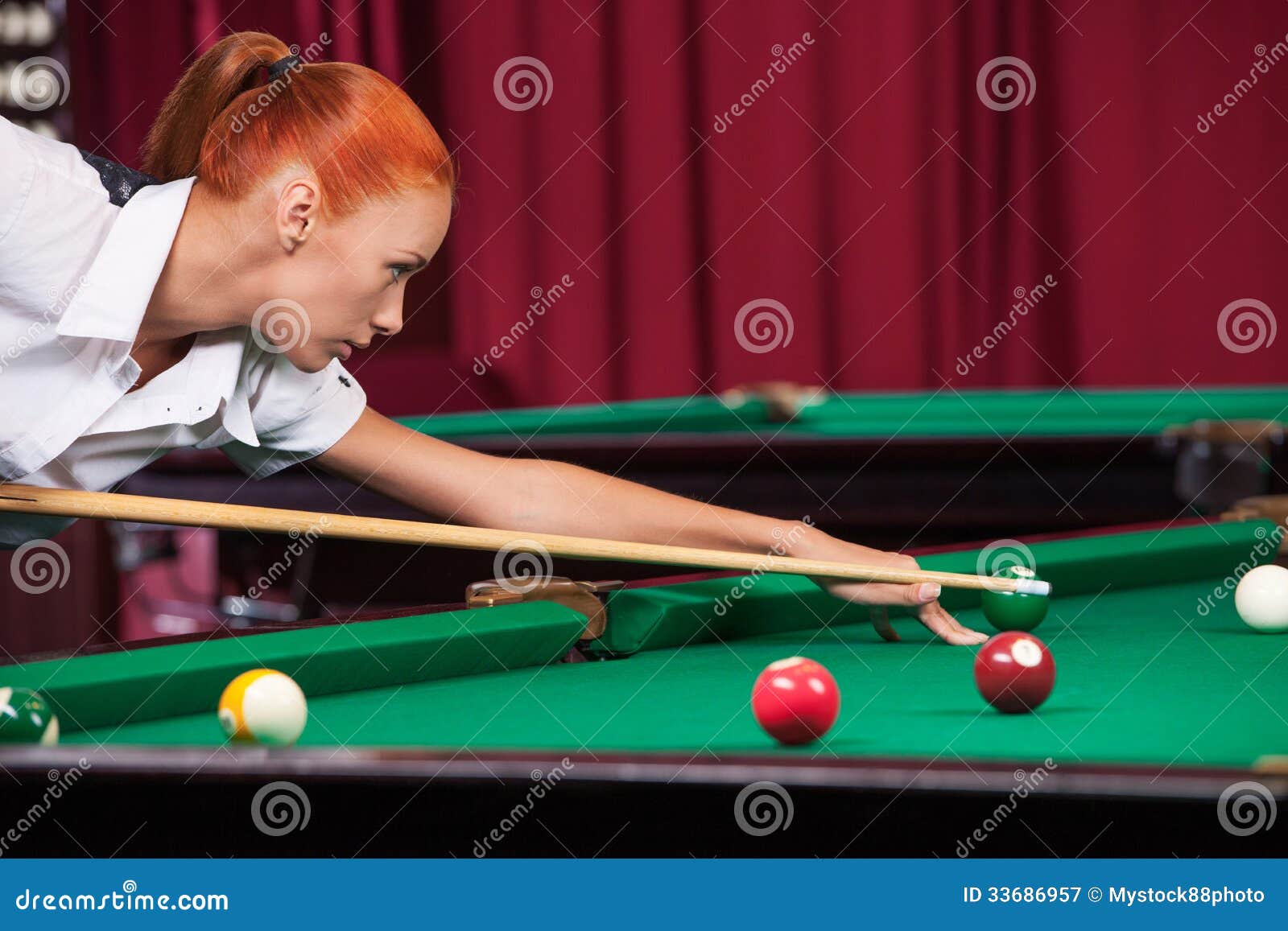 Donna che gioca stagno. Vista laterale della giovane donna sicura che tende la palla da biliardo con la stecca