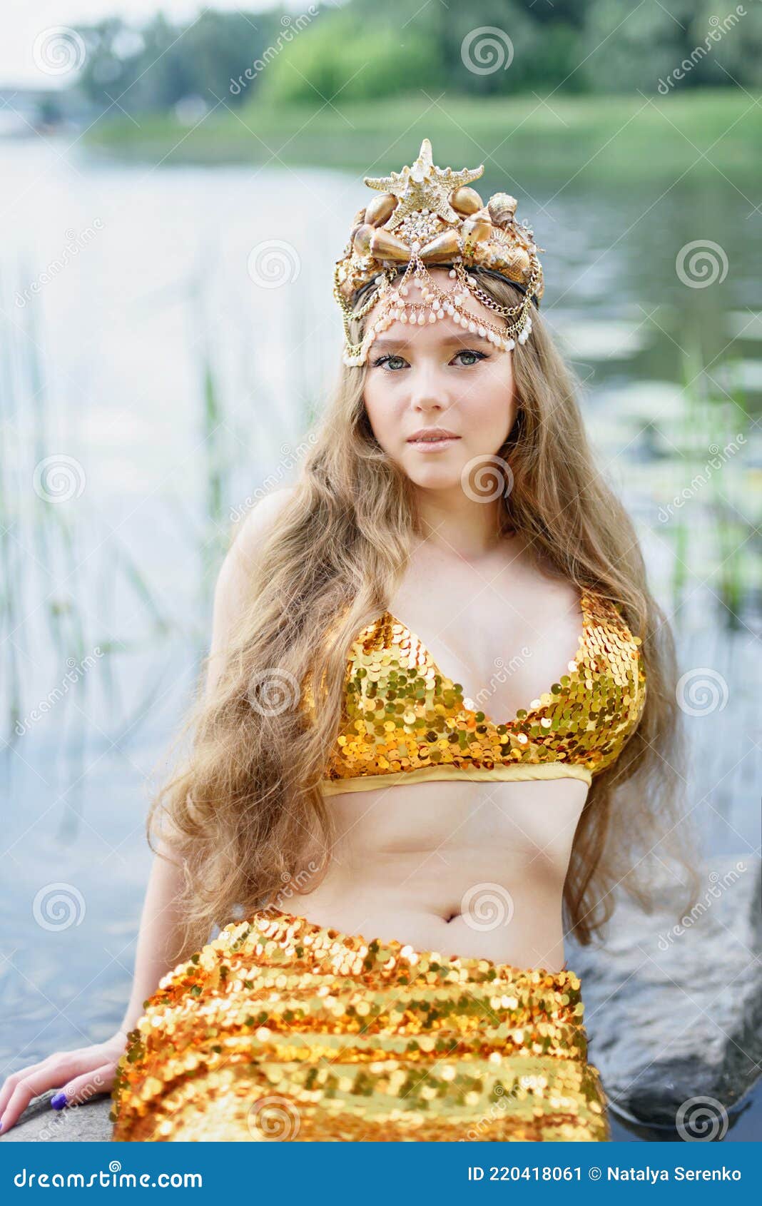 Fantasy donna vera sirena con tridente mito dea del mare con coda dorata  seduta al tramonto su rocce. Oro conchiglie corona gioielli perle. Merma  Foto stock - Alamy