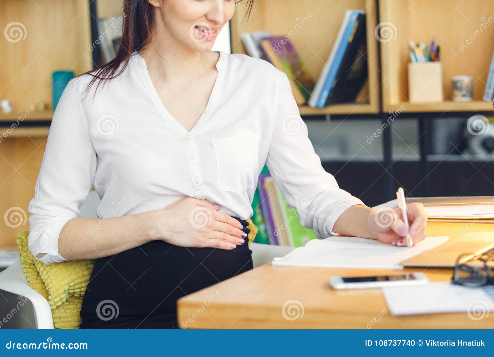 Donna incinta di affari che lavora al primo piano di seduta di scrittura di maternità dell'ufficio. Lavoro femminile incinto all'ufficio all'interno che si siede scrittura che prende il primo piano felice sorridente delle note