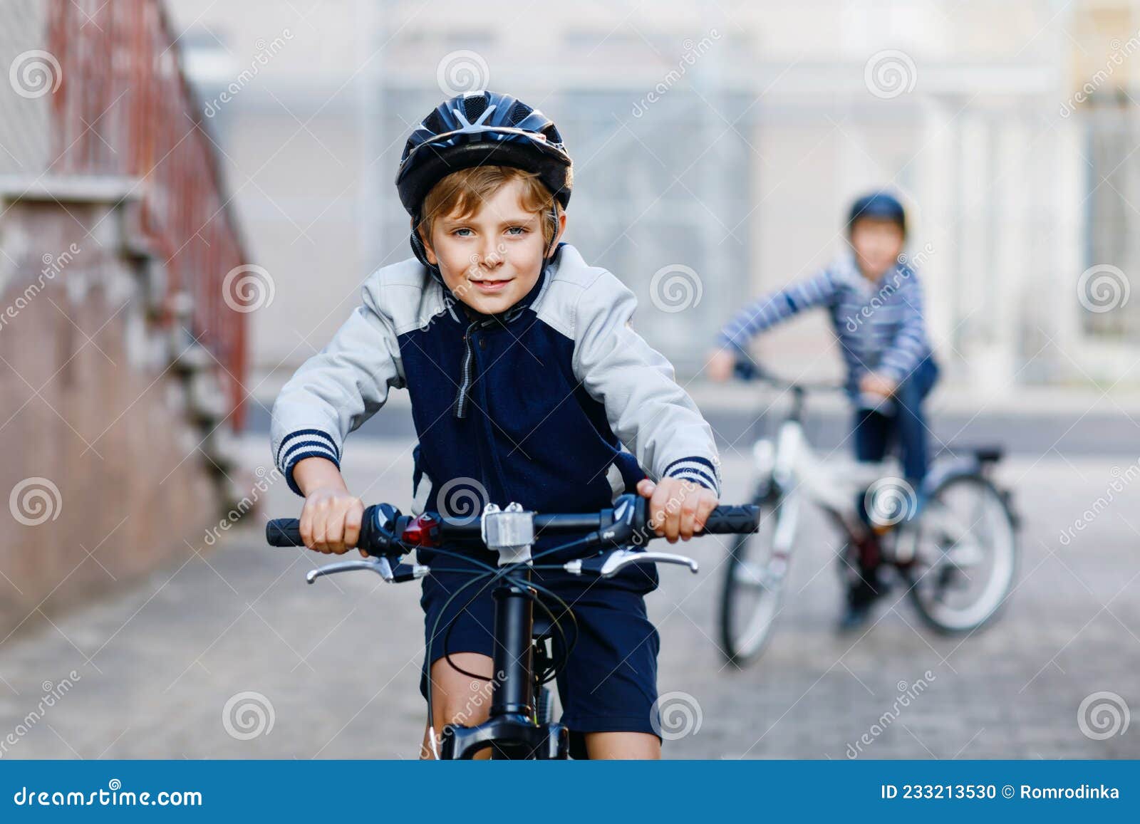 Dos Escolares Con Casco Seguro Montando Bicicleta En La Ciudad Con Mochilas. Niños Felices Con Ropa Colorida Foto de archivo - de conducir, camino: 233213530