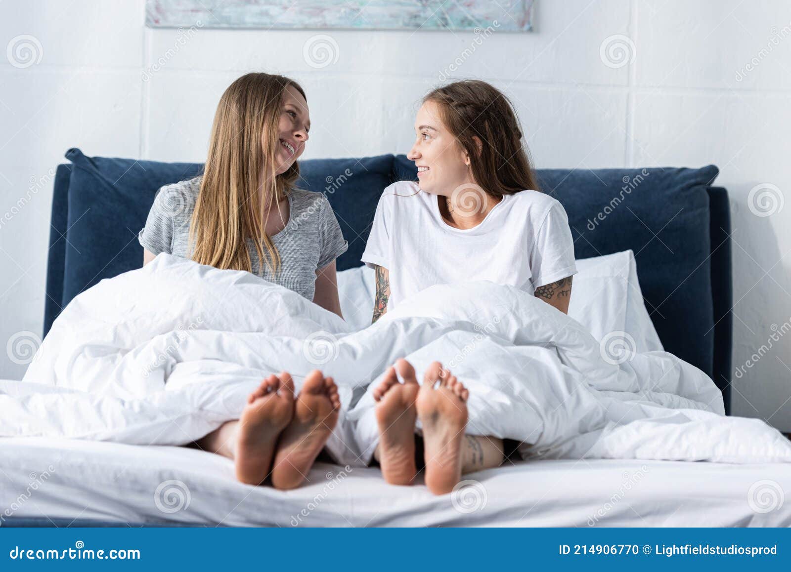 Dos Lesbianas Descalzas Sonrientes Sentadas En La Cama Y Mirándose