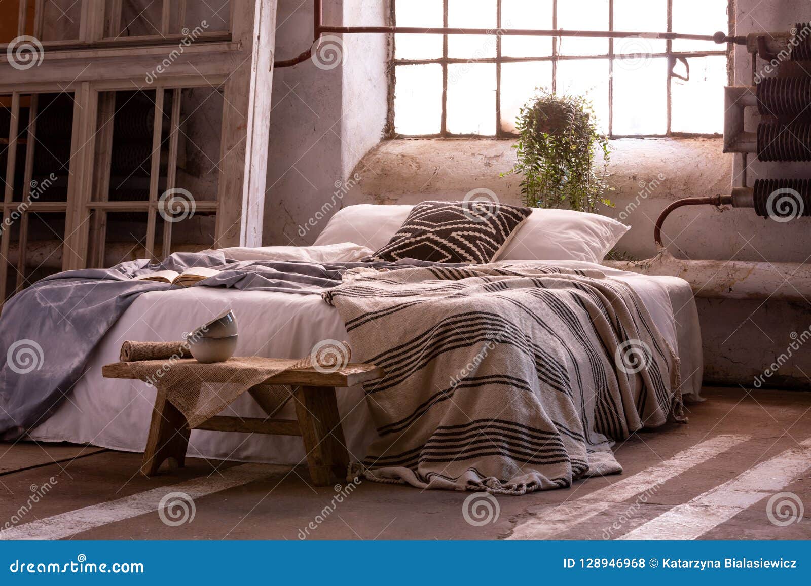 bed with pillows and blanket, wooden stool and plant in a wabi sabi bedroom