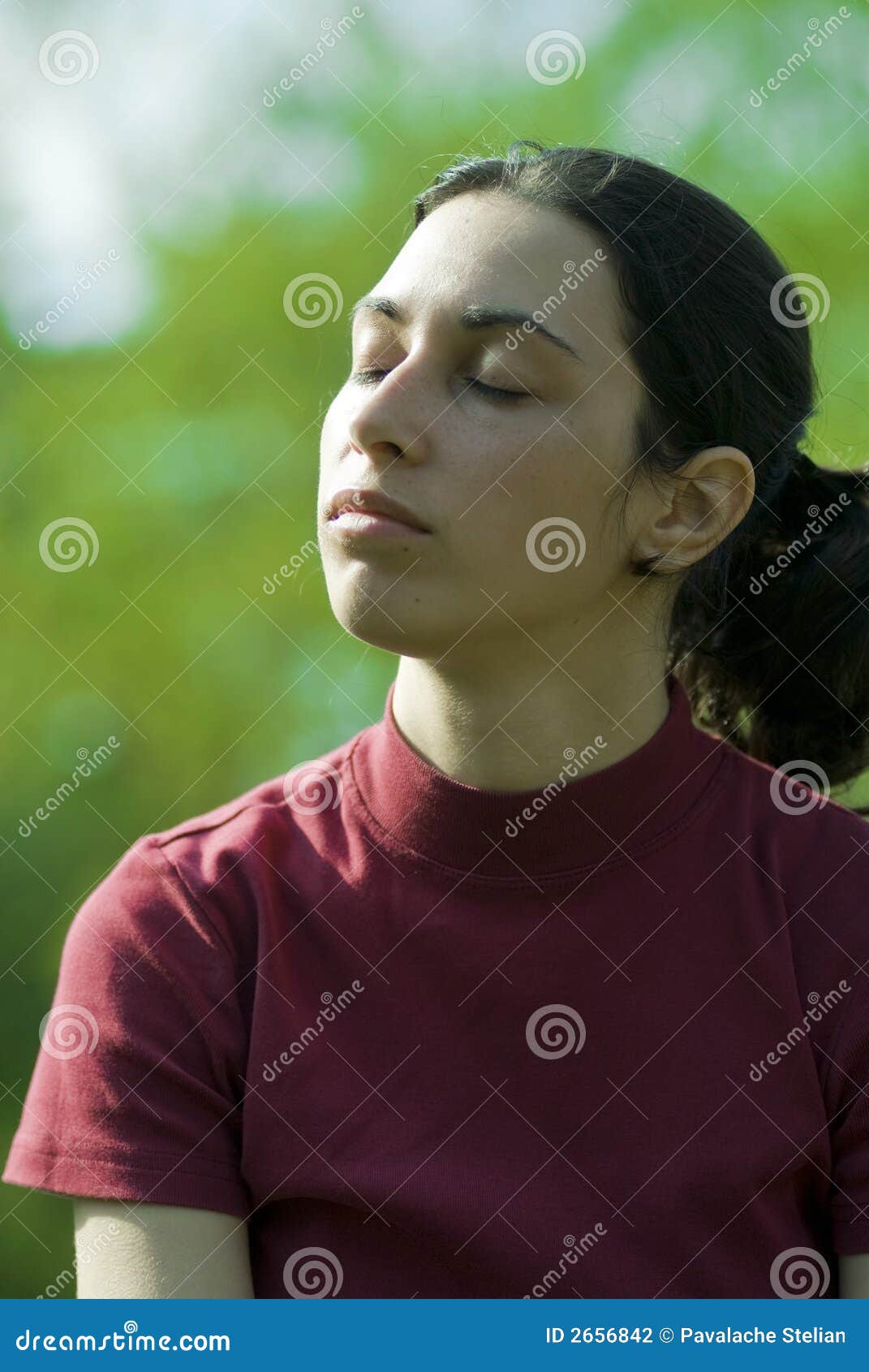 Dreaming away. Young girl with closed eyes dreaming in green field. Vegetation visible in the background.