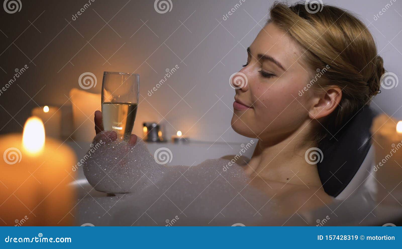 Dreamy Woman Lying In Bath With Foam Bubbles And Candles Drinking