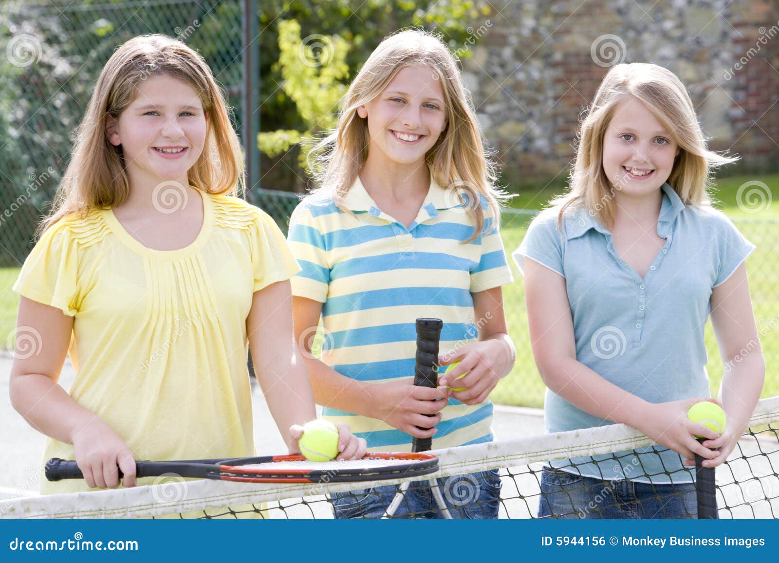 Drei junge Freundinnen auf dem Tennisgerichtslächeln. Drei junge Freundinnen mit Schlägern auf dem Tennisgerichtslächeln