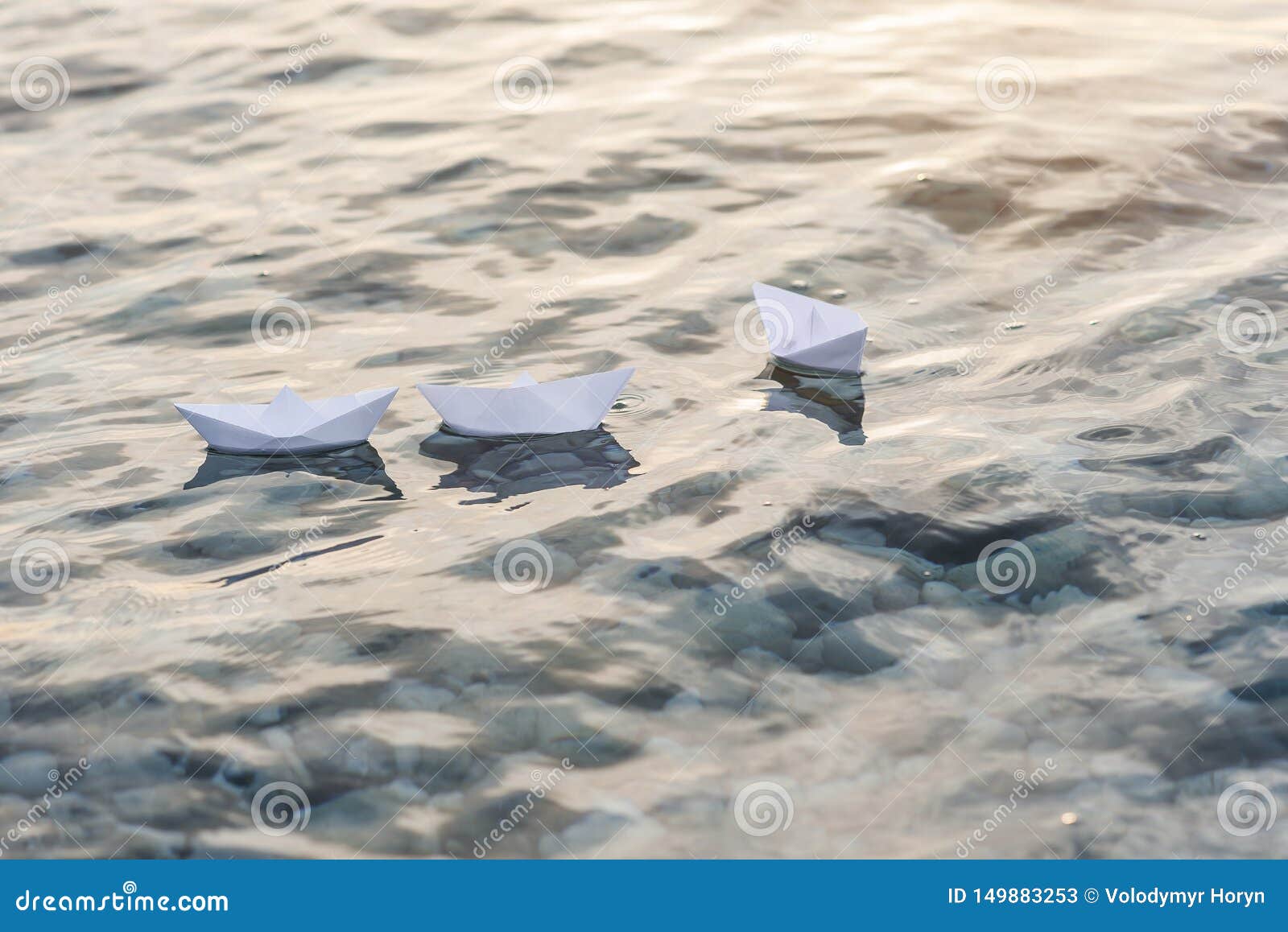 Drei Papierboote, die in Wellen auf dem Wasser bei Sonnenuntergang schwimmen. Gruppe von drei Papierbooten, die in Wellen auf dem Wasser bei Sonnenuntergang schwimmen