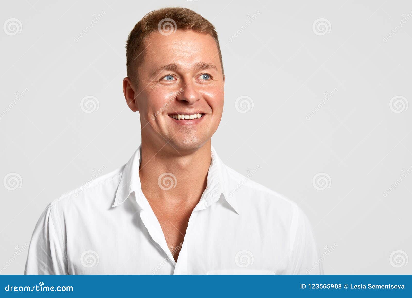 dremy blue eyed male with positive expression, broad smile, shows white teeth, looks into distance, thinks about something, wears