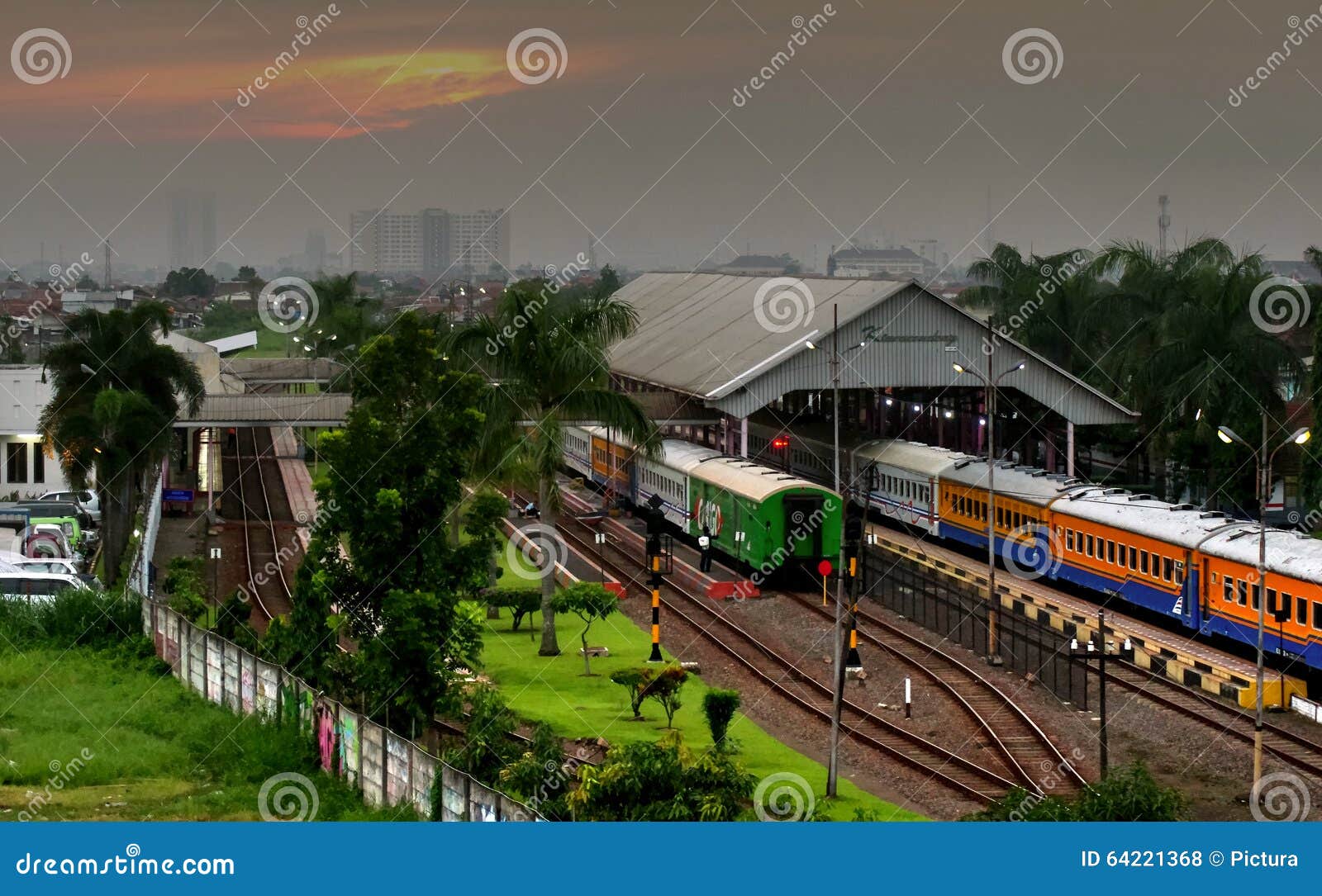 Drev i den Bandung järnvägsstationen. Bandung järnvägsstation, Indonesien, på solnedgången med passageraredrev som stoppas på två plattformar och broar över ett annat spår, bakgrund av träd