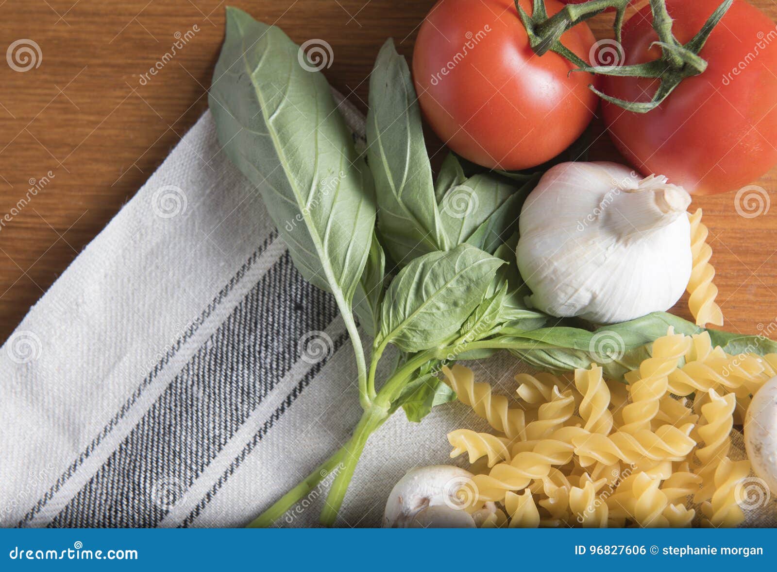 Dried fusilli pasta with tomatoes, basil and garlic on a wooden background