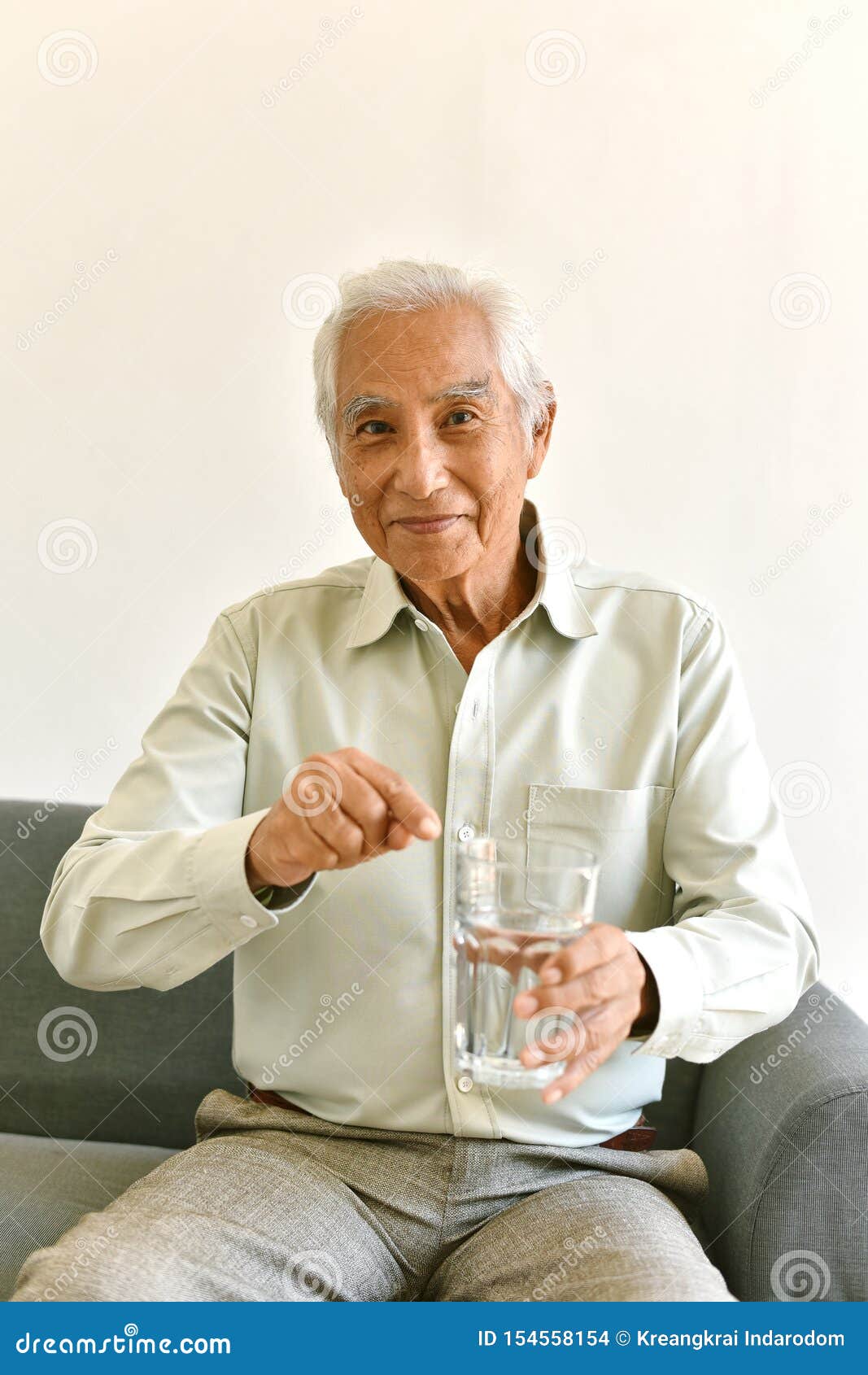 drinking water is good healthy habit for old man, elderly smiling asian man pointing at glass of purified water.