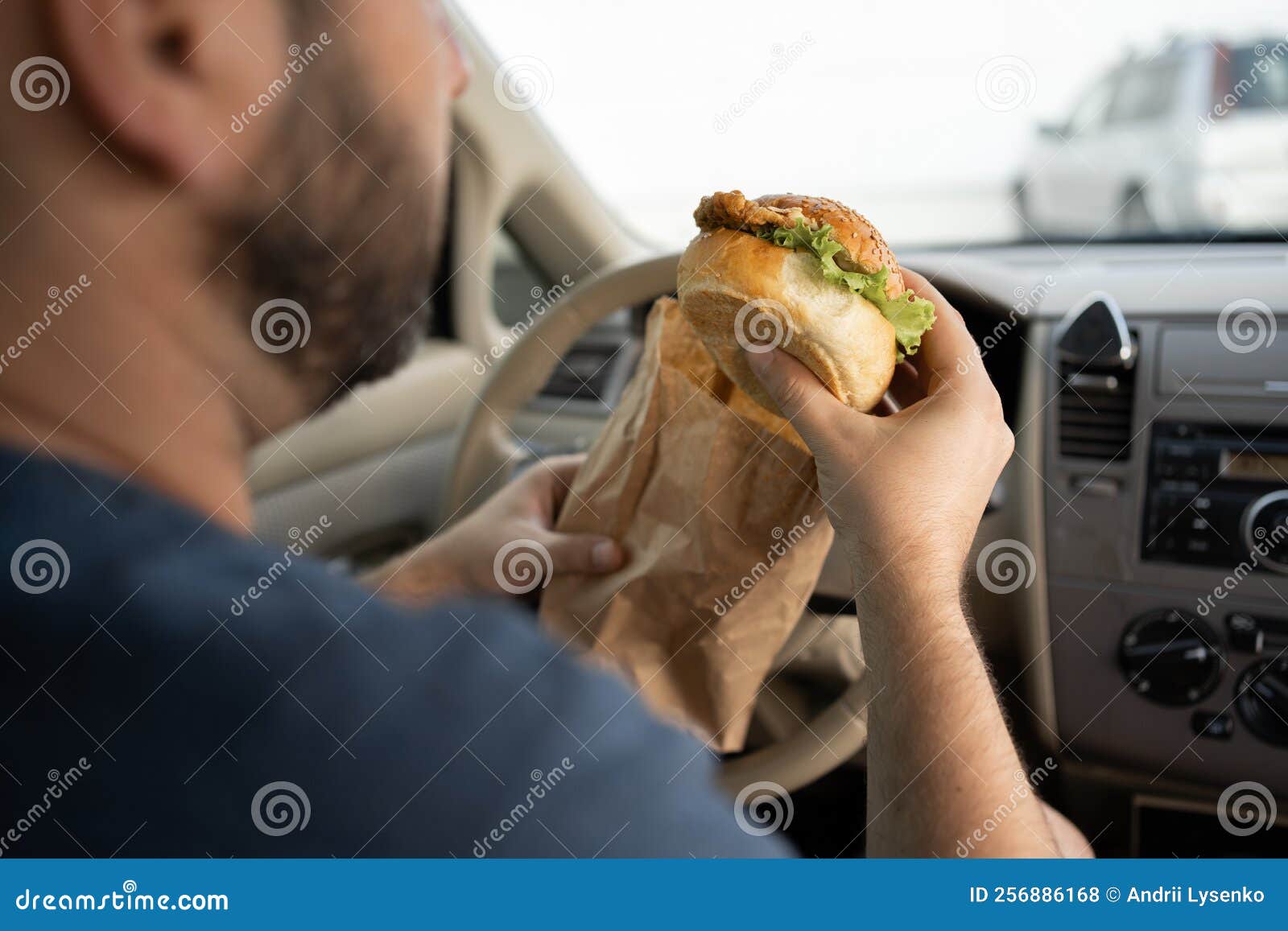 The Driver Eating a Hamburger in the Car. Breakfast Burger in a Traffic