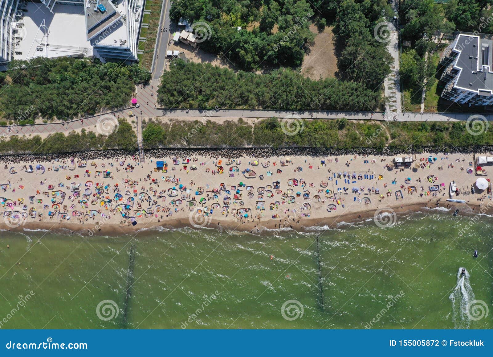 drone aerial top down view on sunny beach with sunbathers with windbreaks and towels at sea in touristic city