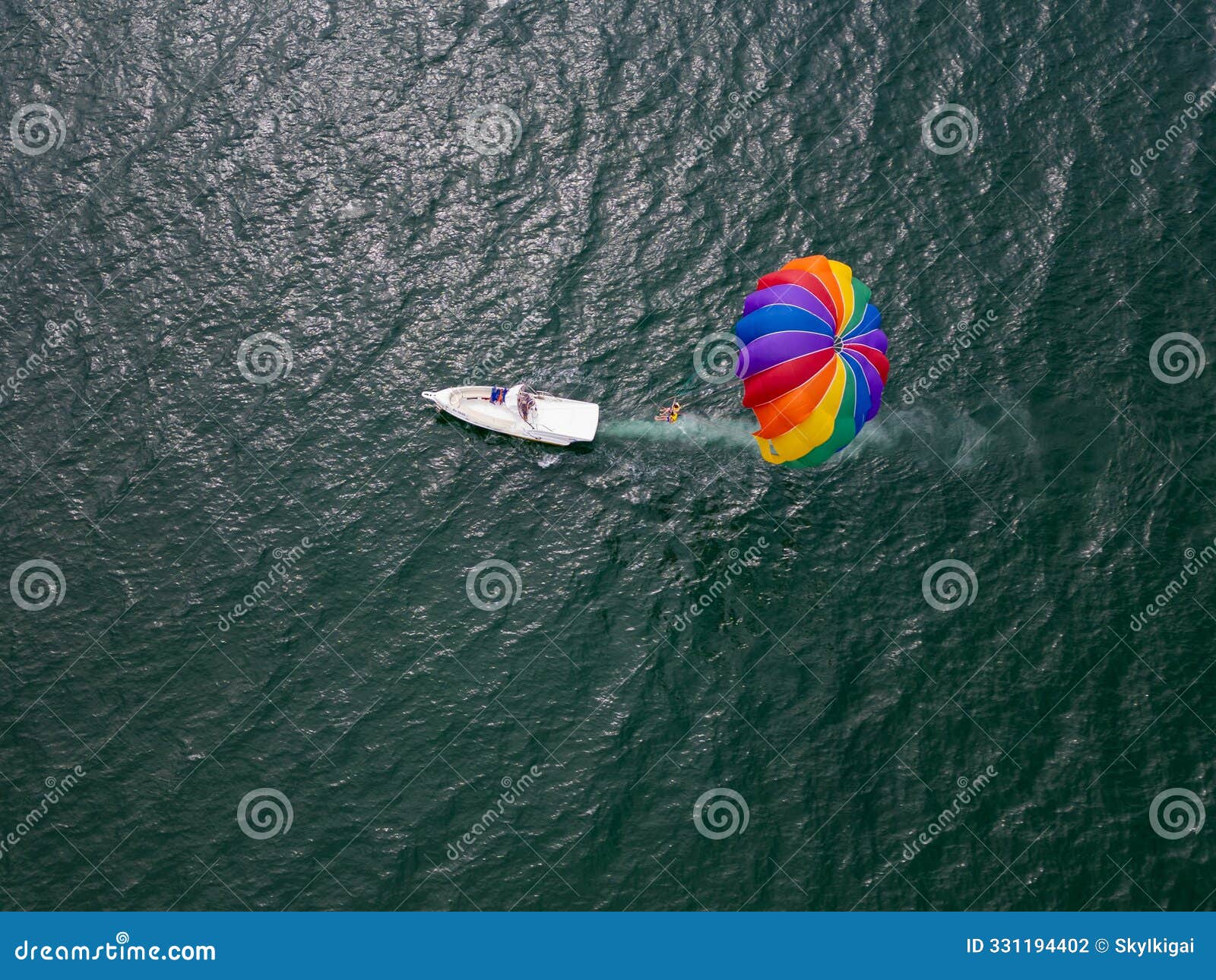 drone video of a colorful parasail soaring over the open ocean, towed by a speedboat below. the aerial view captures the