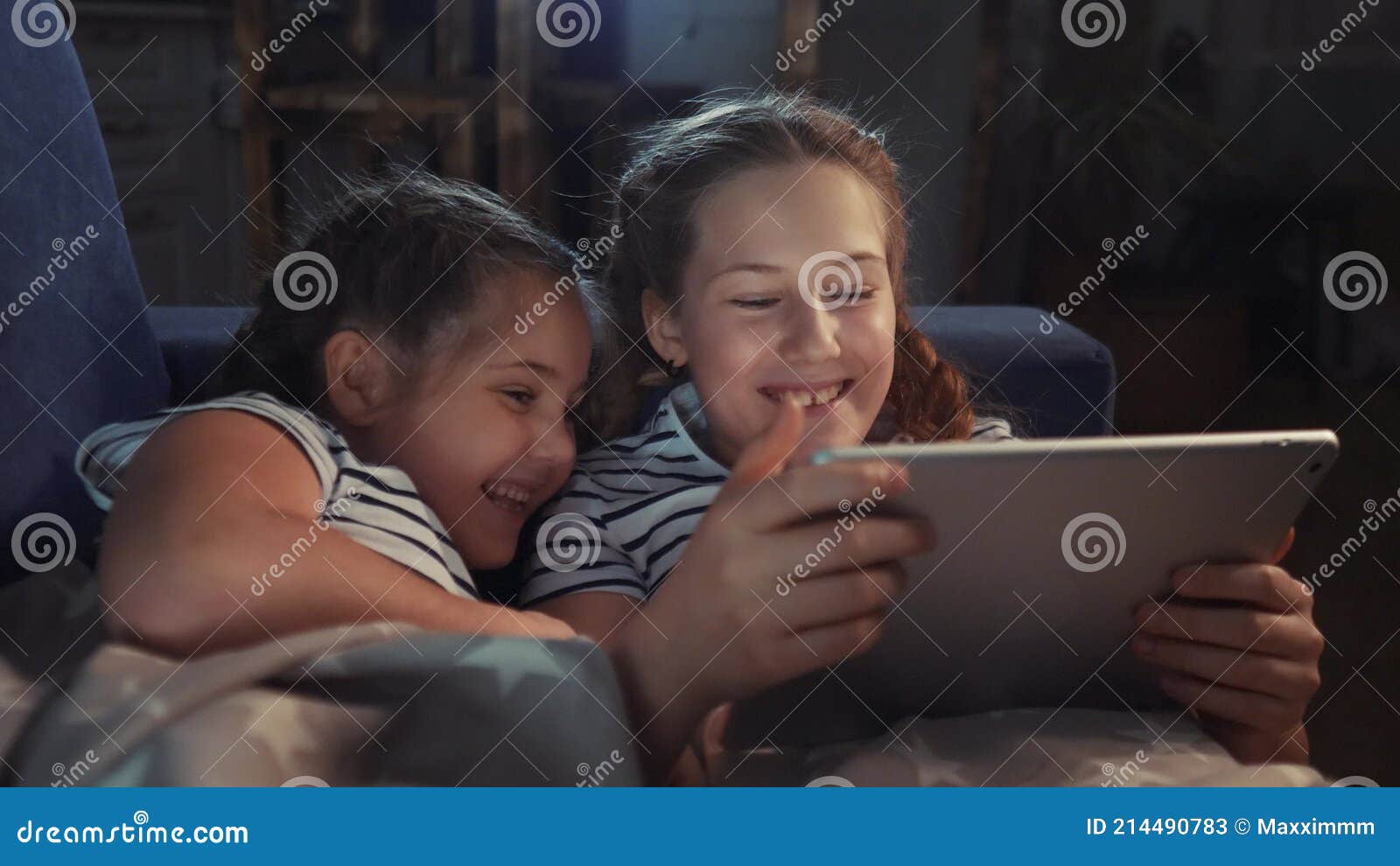 Duas Meninas No Sofá à Noite Com Um Tablet Digital. Jogos