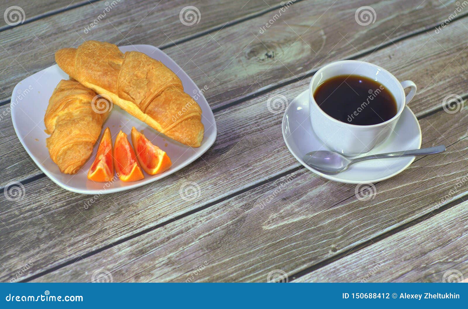 Due croissant con le fette arancio su un piatto e su una tazza di caffè nero su un piattino con un cucchiaio sulla tavola Primo p