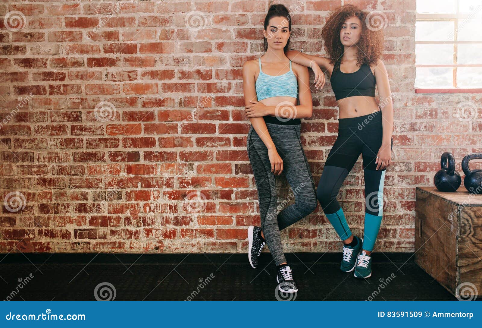 Un colpo integrale di due giovani donne che fanno una pausa parete in palestra Femmine di forma fisica che si rilassano all'allenamento