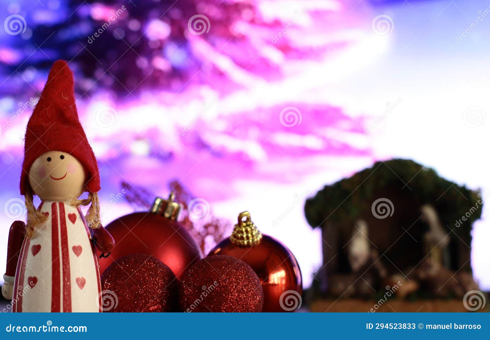 duende navideÃ±o con bols de navidad rojas brillantes y mates con portal de belen y arbol nevado de fondo.