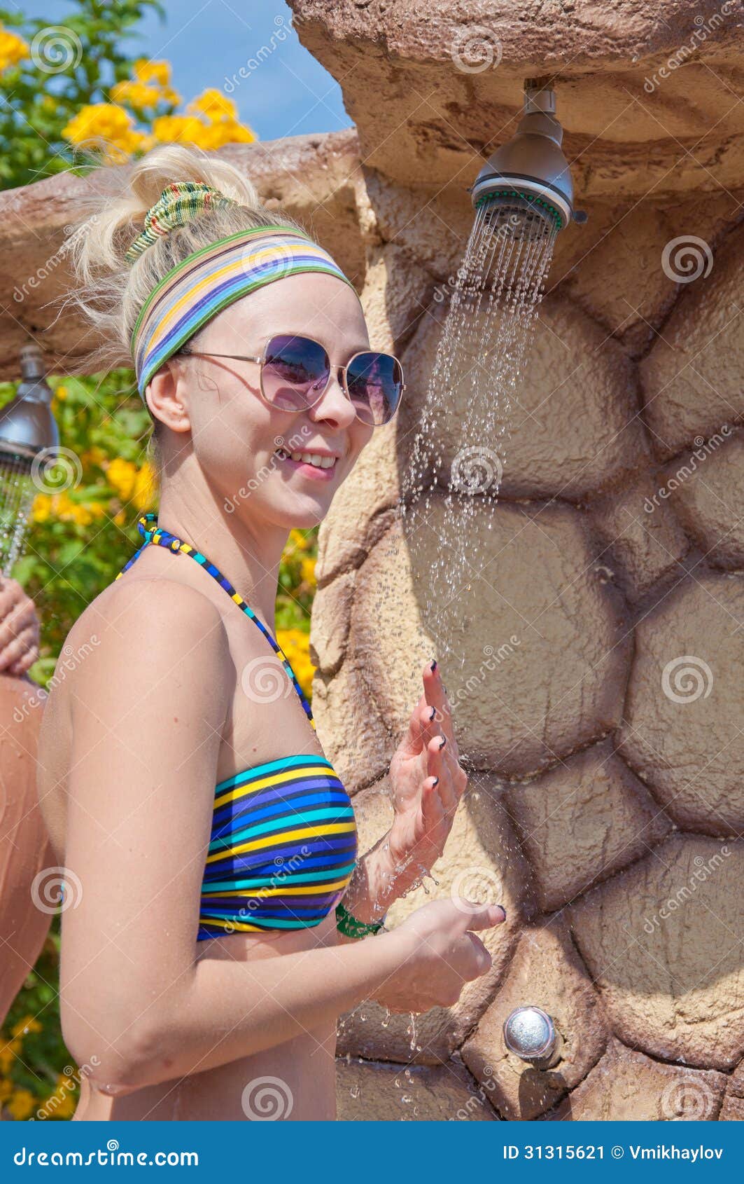 Junge schöne lächelnde gebräunte blonde Frau im Bikini an der Dusche auf einem Seestrand