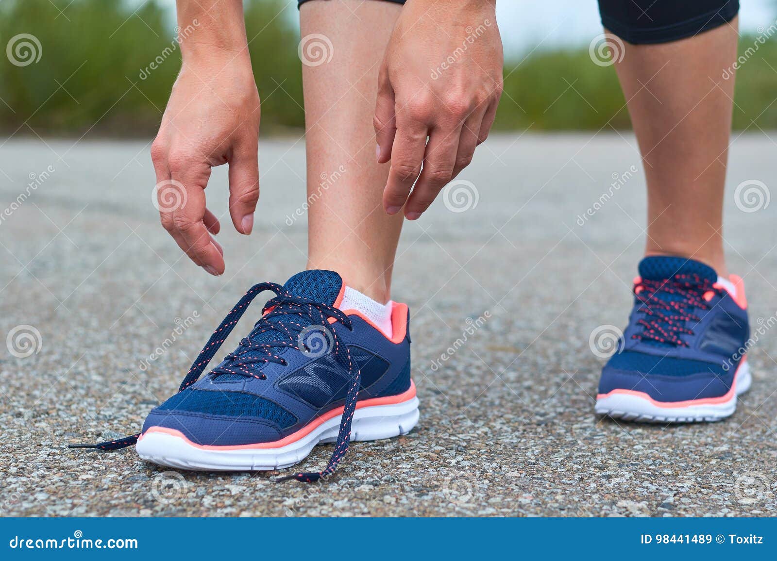 Dziewczyna wiąże up shoelaces w sneakers na drodze podczas gdy jogging, nogi i sneakers,