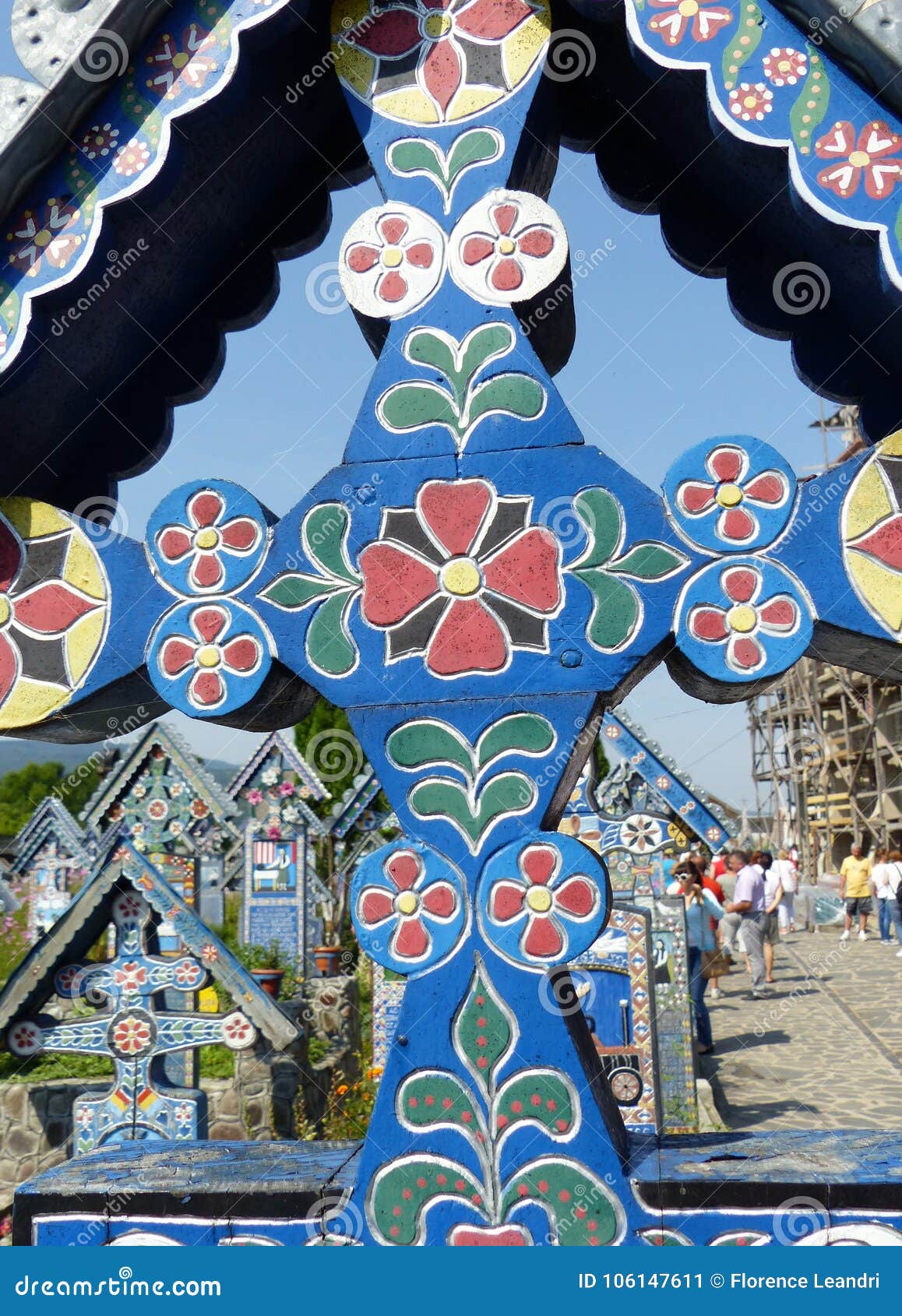 Détail d'une croix en bois décorée du joyeux cimetière célèbre de Sapanta en Roumanie. Détail d'une croix en bois décorée Cimetière célèbre de joyeux cimetière de Sapanta en Roumanie course de agrandissement en verre de carte de destination Ciel clair bleu Jour ensoleillé temps de vacances Jeunes adultes Croix bleue avec des croquis colorés Croquis sous la forme de fleurs et de feuilles Couleurs bleues, vertes, rouges, jaunes et blanches Les gens dans la distance Autre a décoré des croix dans la distance Cimetière unique Le rapresentazione du ` s de la mort avec joie n