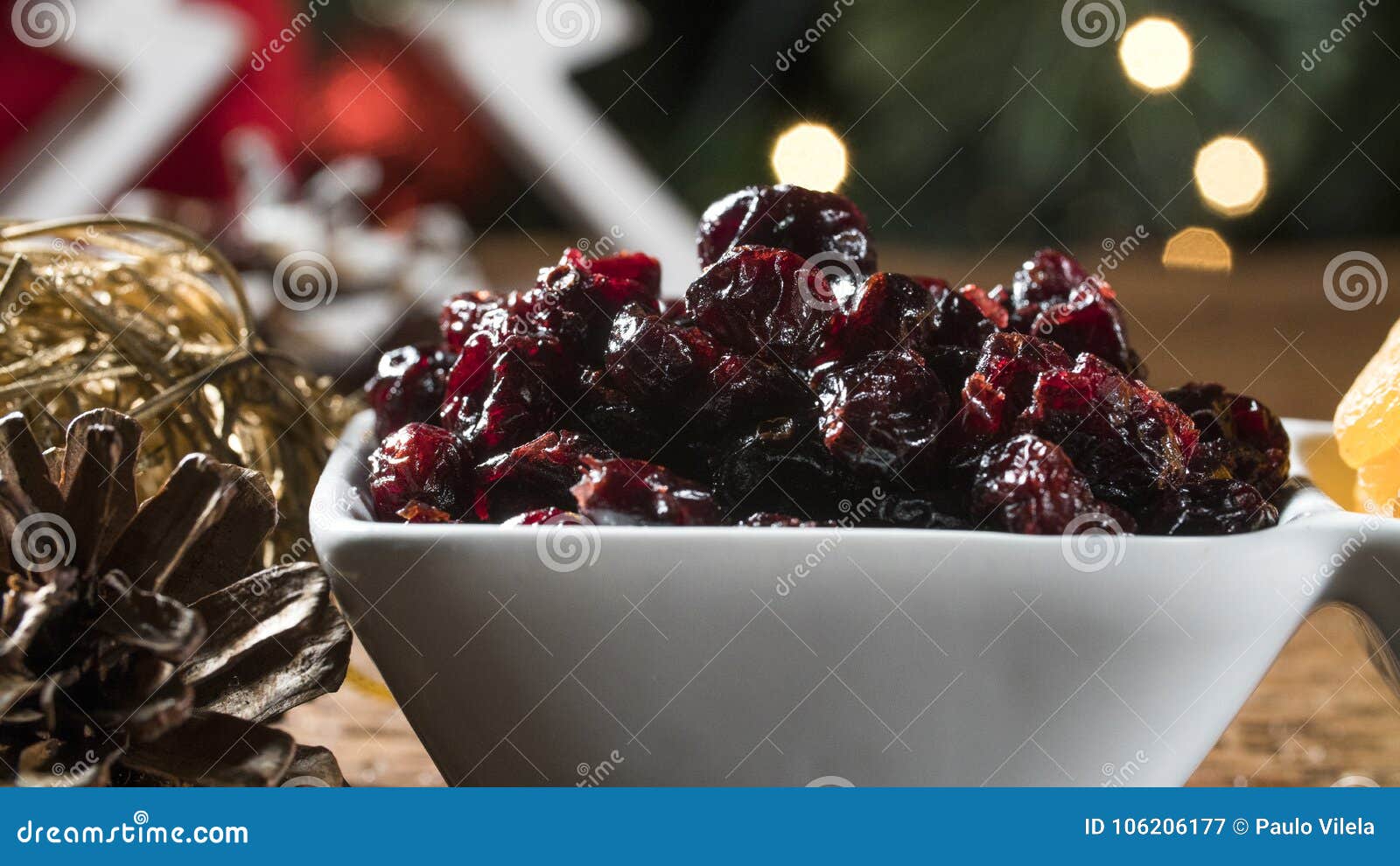 Dried apricots, pitted and dried berry in a bowl on the board with blurred christmas background.