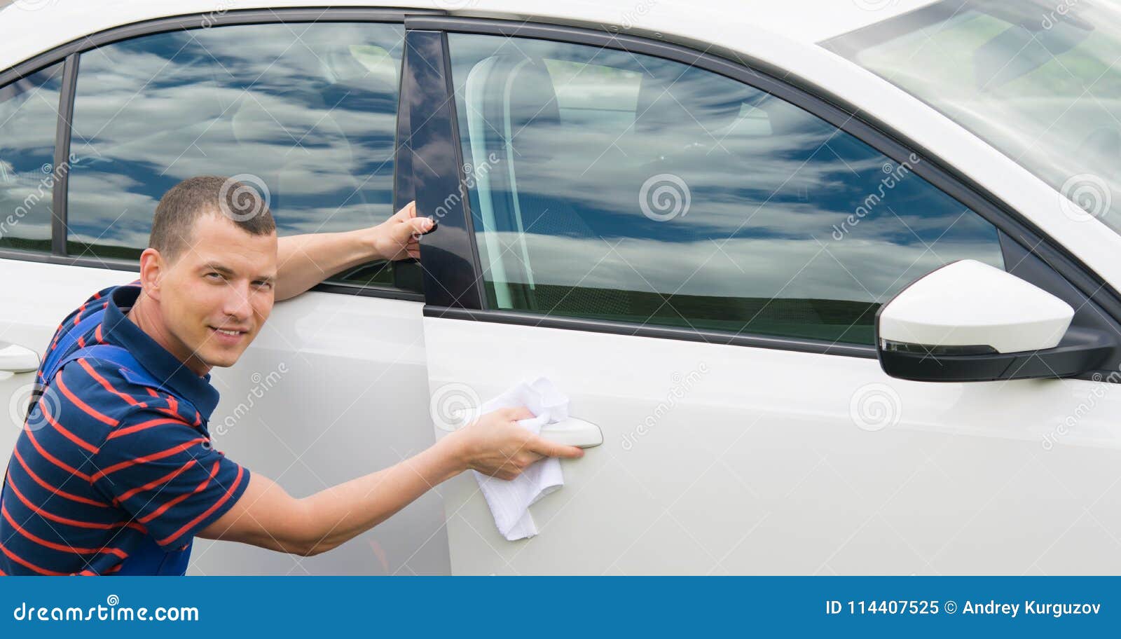 Worker in a blue suit smiles and wipes the car with a white rag