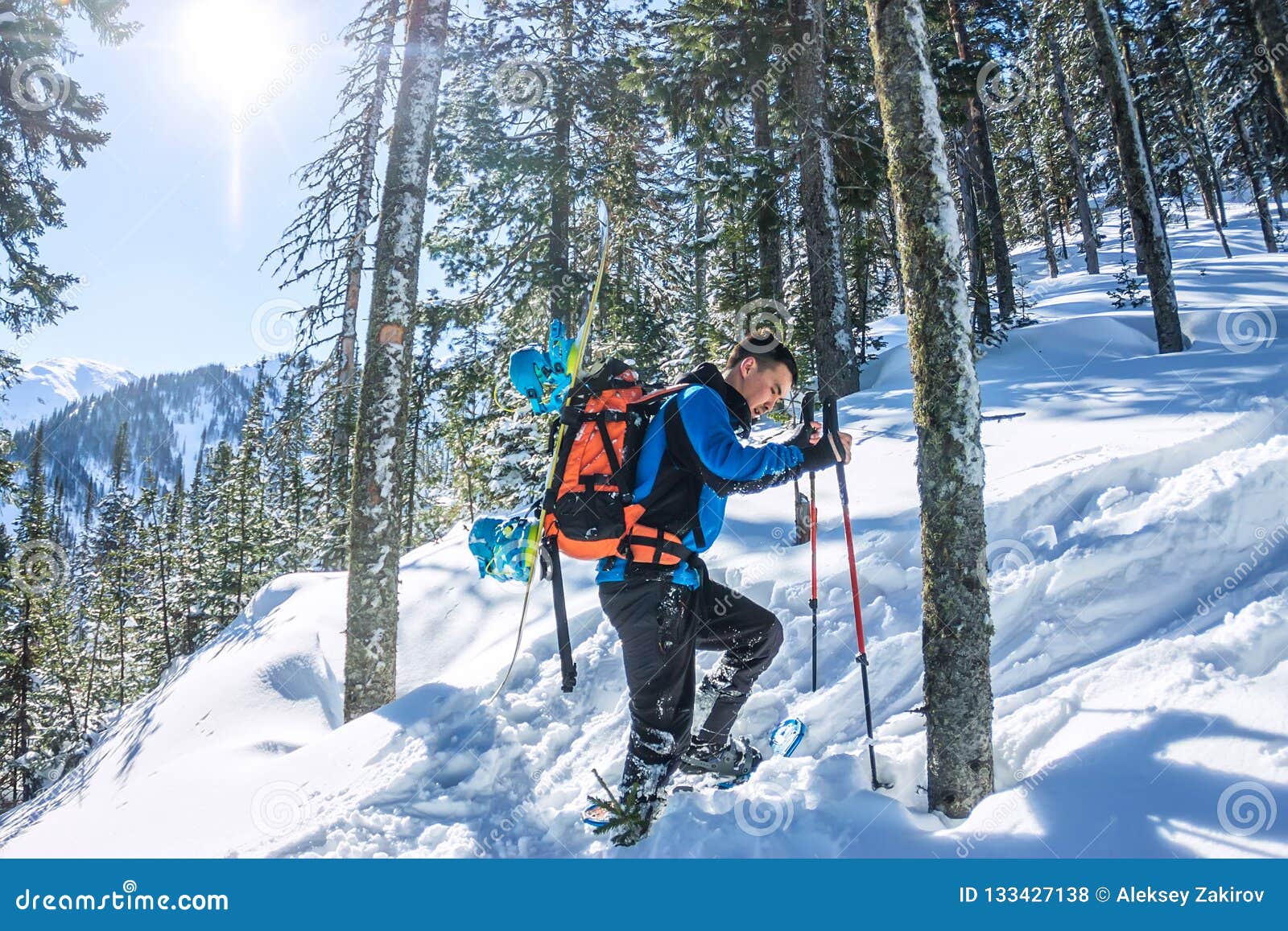 Asian Man Snowboarder Freeride in Snowshoes Rises Uphill in Winter on