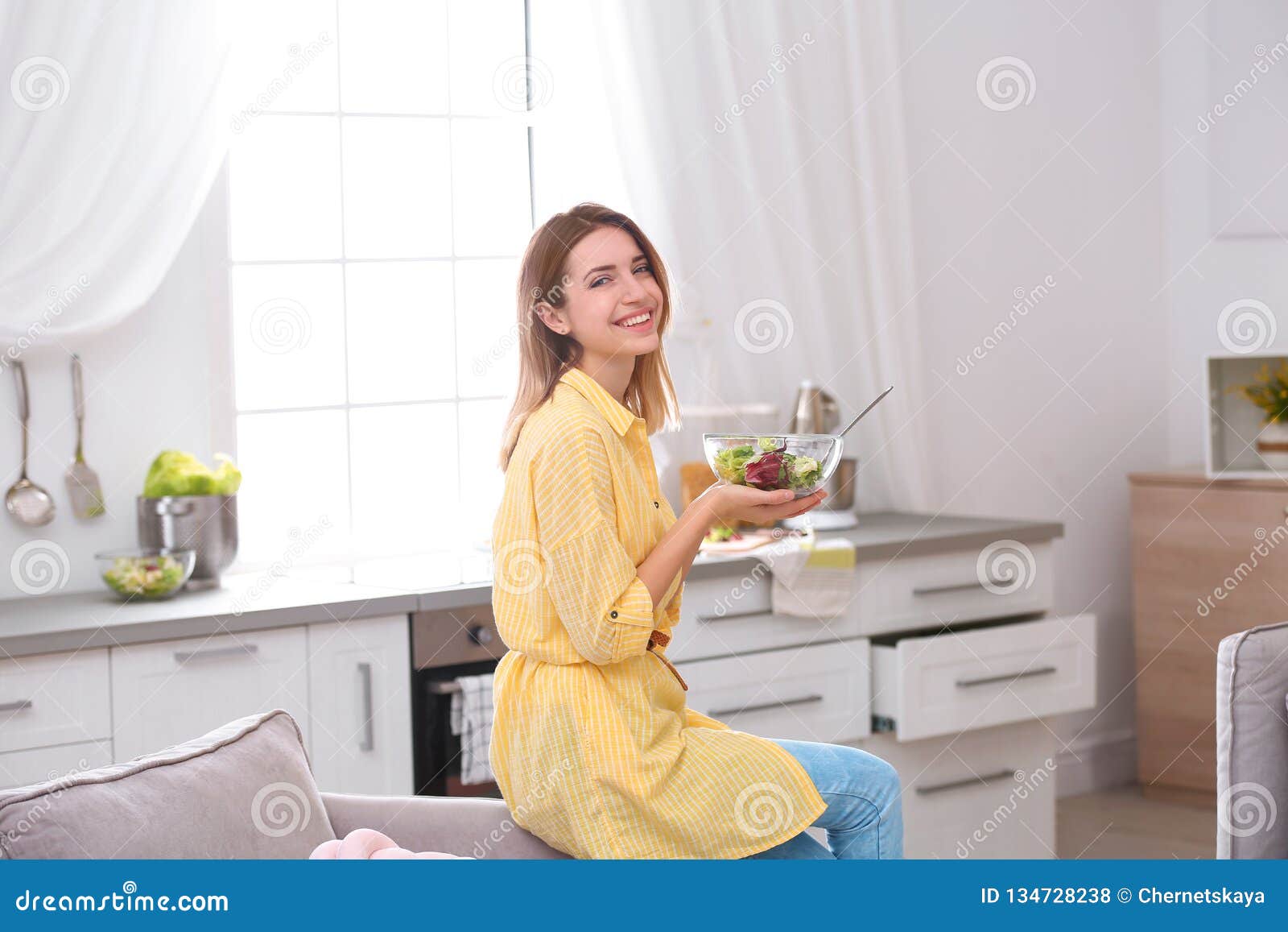 Happy young woman eating salad in kitche. Lycklig ung kvinna som äter sallad i kök banta sunt
