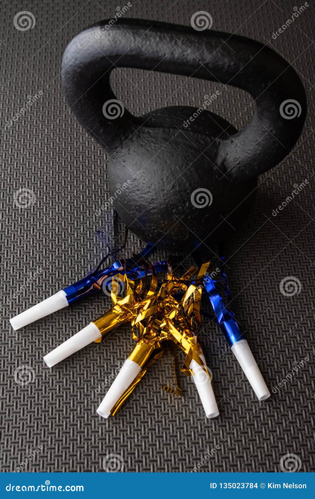 Black kettlebell on a black gym floor with blue and gold noisemakers to celebrate New Yearâ€™s Eve fitness