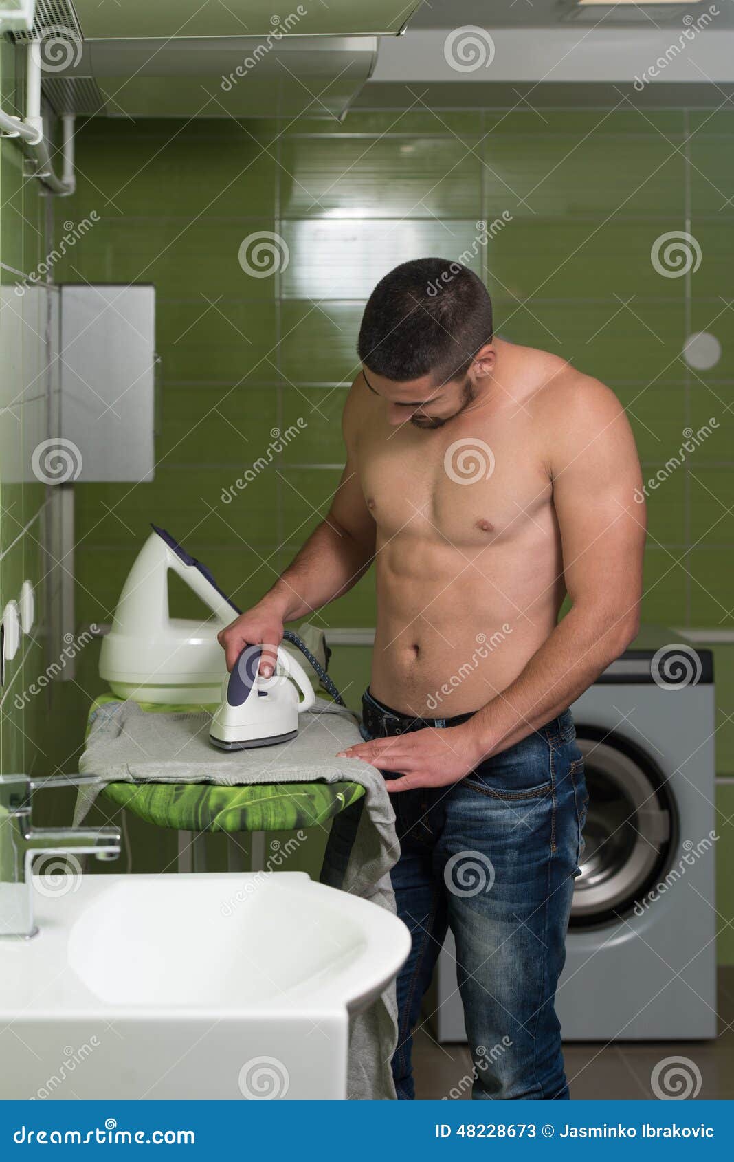 Smiling Man Ironing Clothes At Utility Room. Lavoro domestico rivestente di ferro dei vestiti dell'uomo bello nudo felice