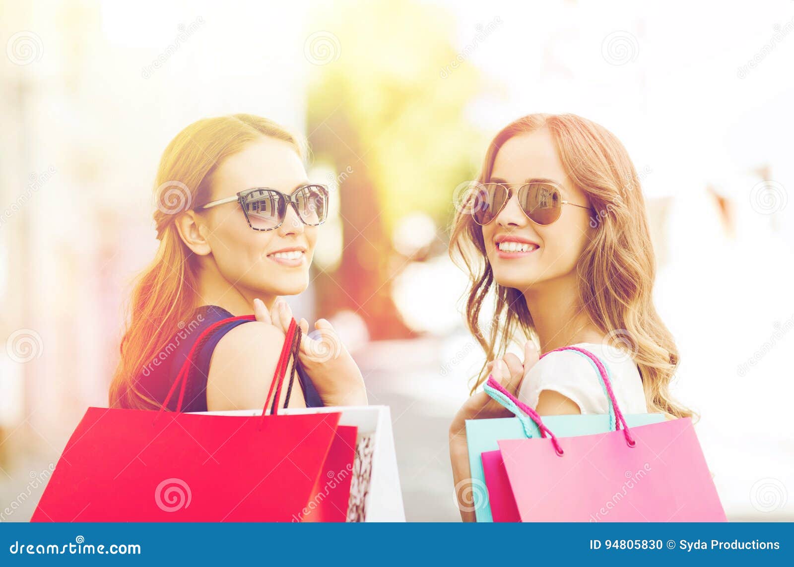 Happy young women with shopping bags in city. Продажа, защита интересов потребителя и концепция людей - счастливые молодые женщины в солнечных очках с хозяйственными сумками на улице города