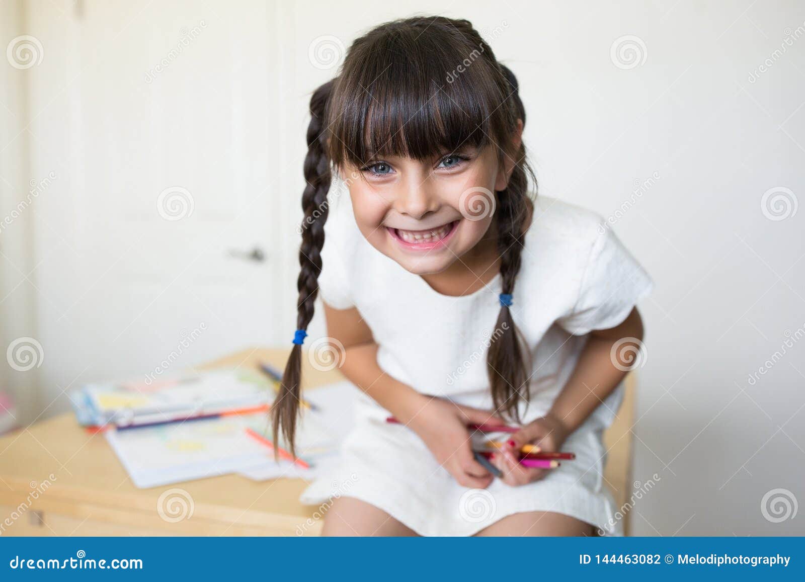 Happy girl with colored pencils in hand. 6-7 years old joyful child looking at the camera and smiling